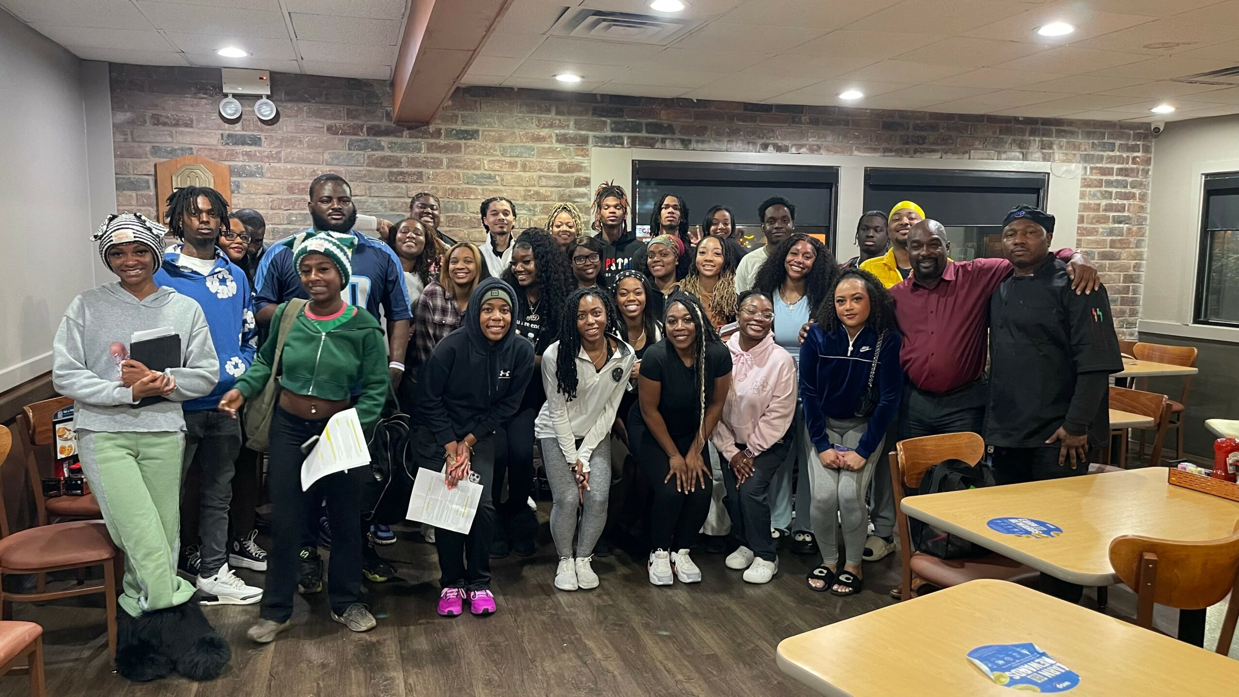 Group of people standing together in a room with brick walls and tables, smiling for the photo.