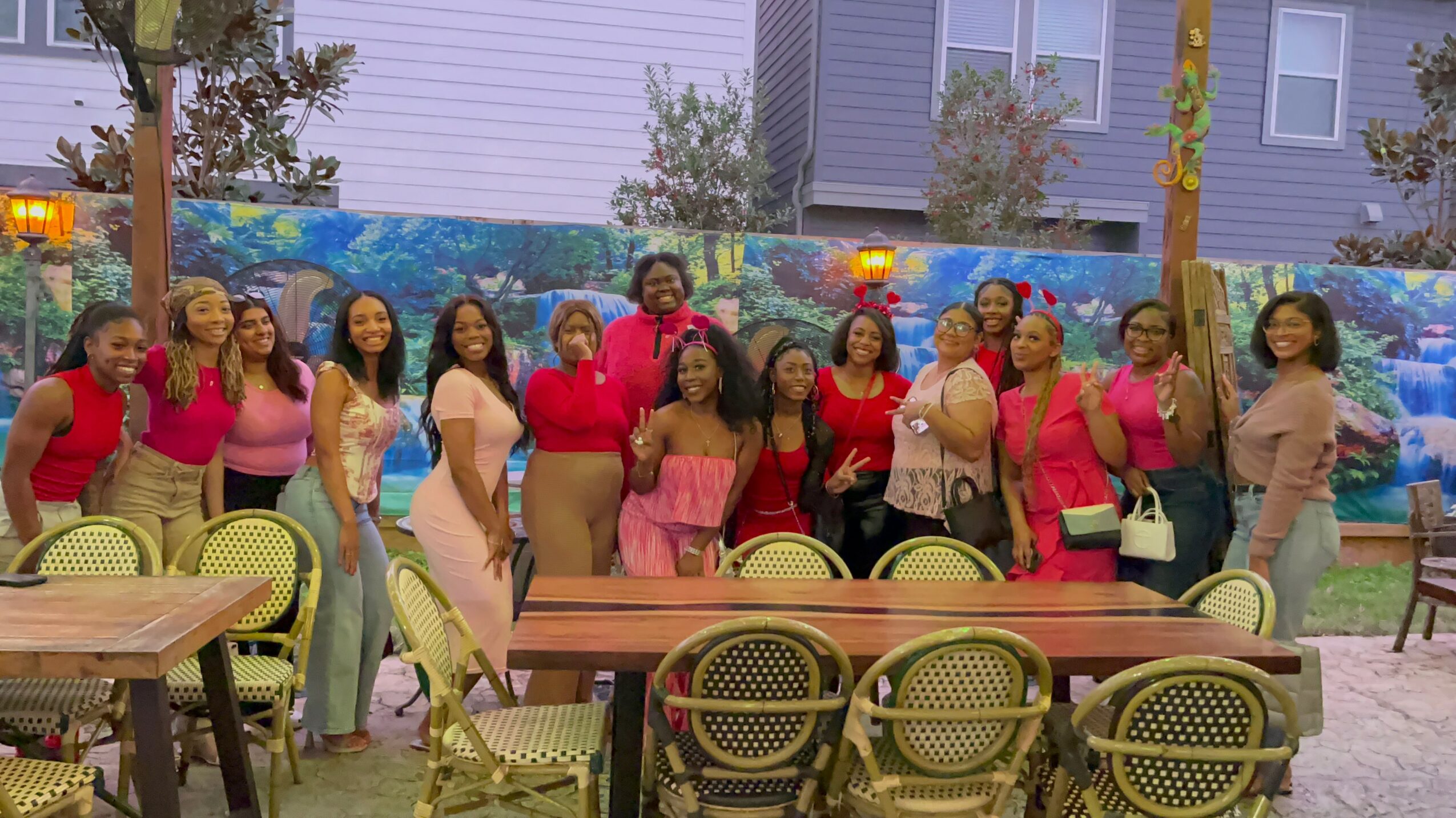 Group of women standing outdoors near tables and chairs, with trees and buildings in the background.