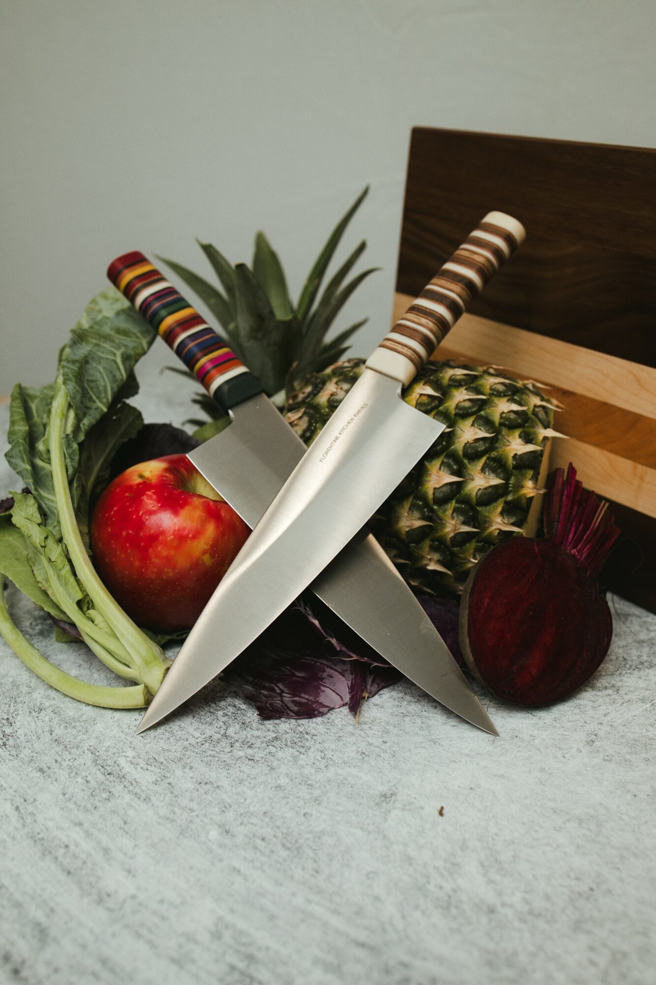 Cutting board with knives, pineapple, apple, beetroot, and leafy greens on a light surface.