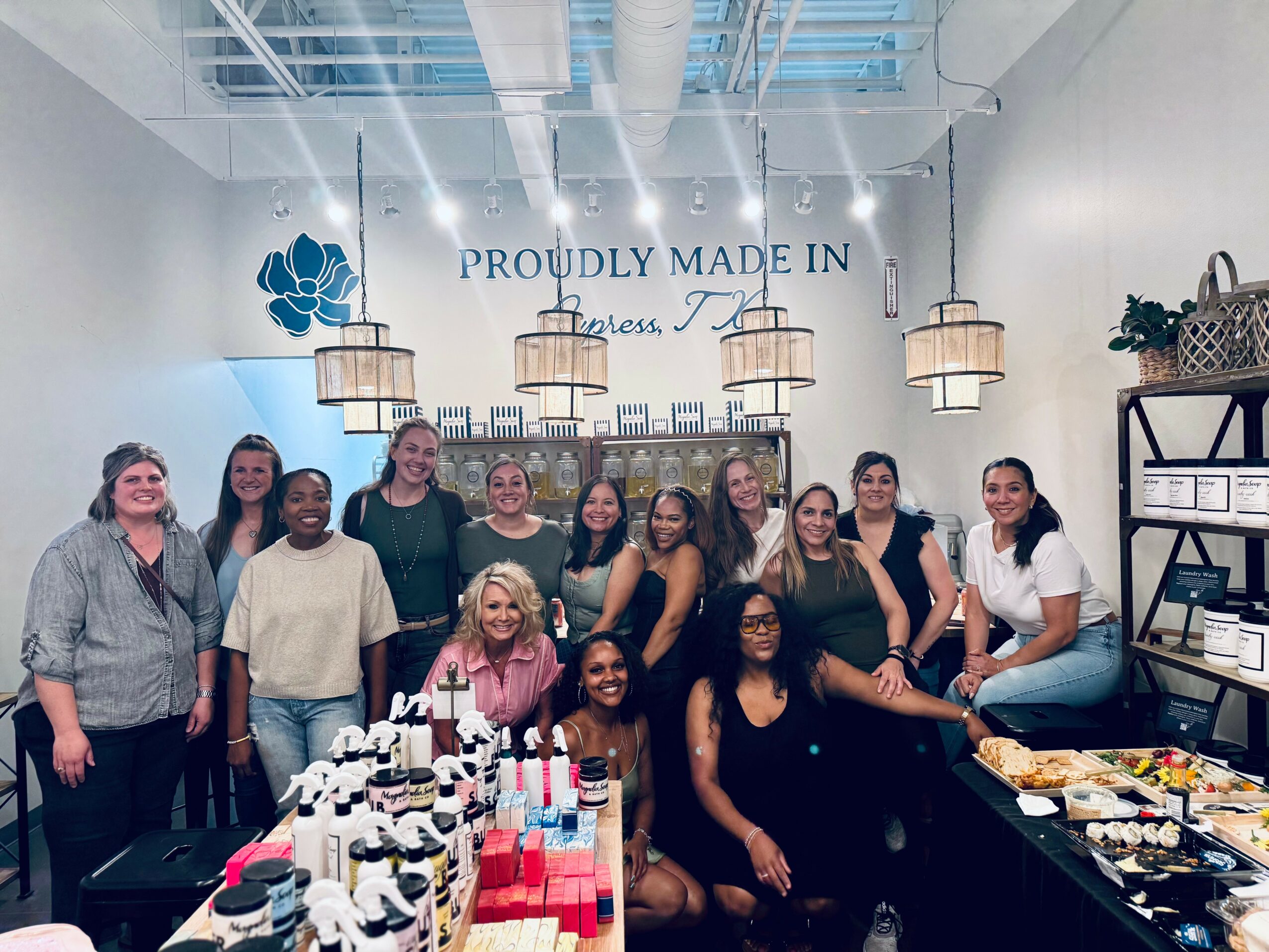 Group of women in a store with hanging lights and shelves, smiling and posing for a photo.