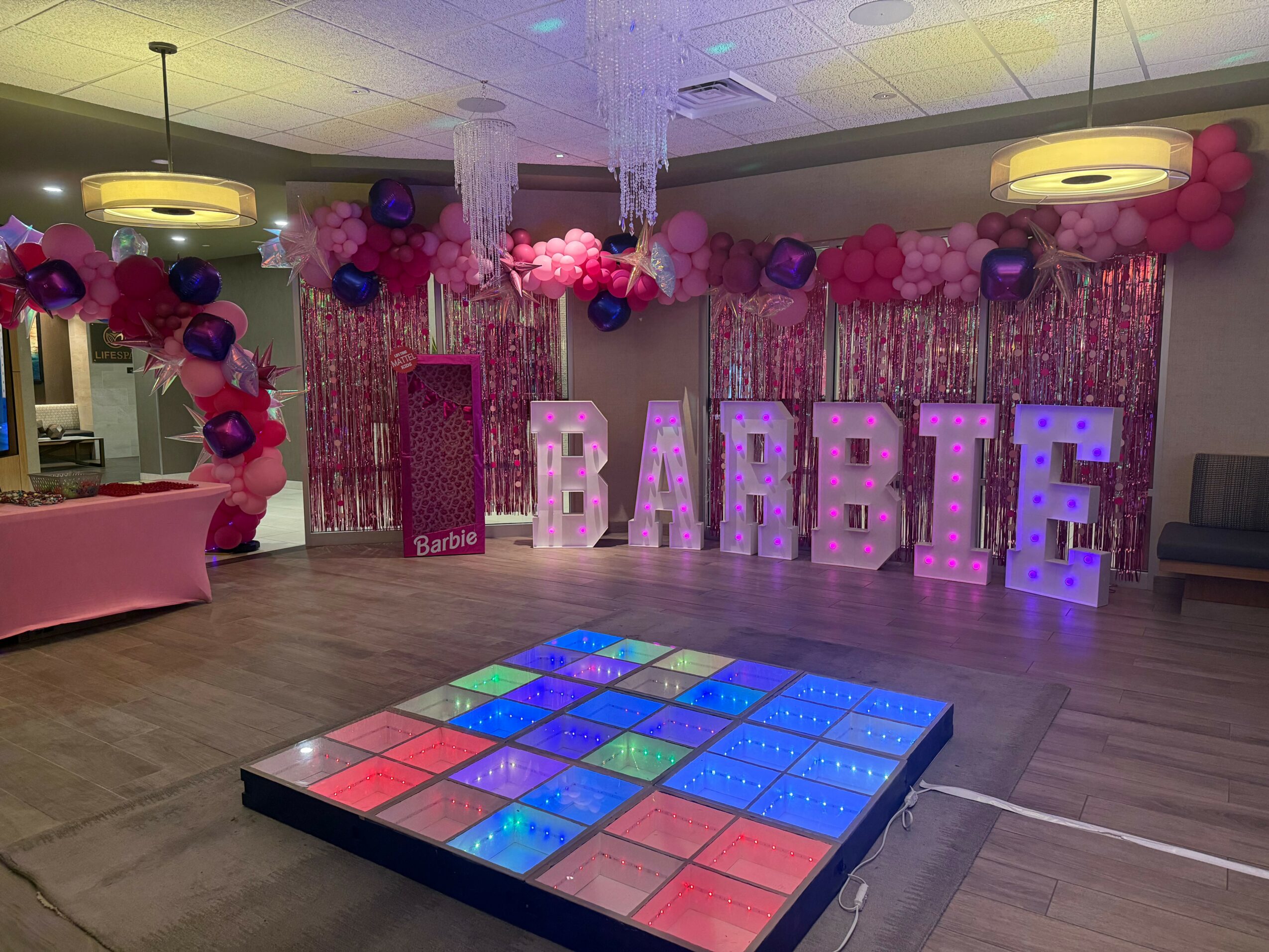 Party room decorated with pink and purple balloons, large illuminated letters spelling 'BABY', and a colorful illuminated floor.