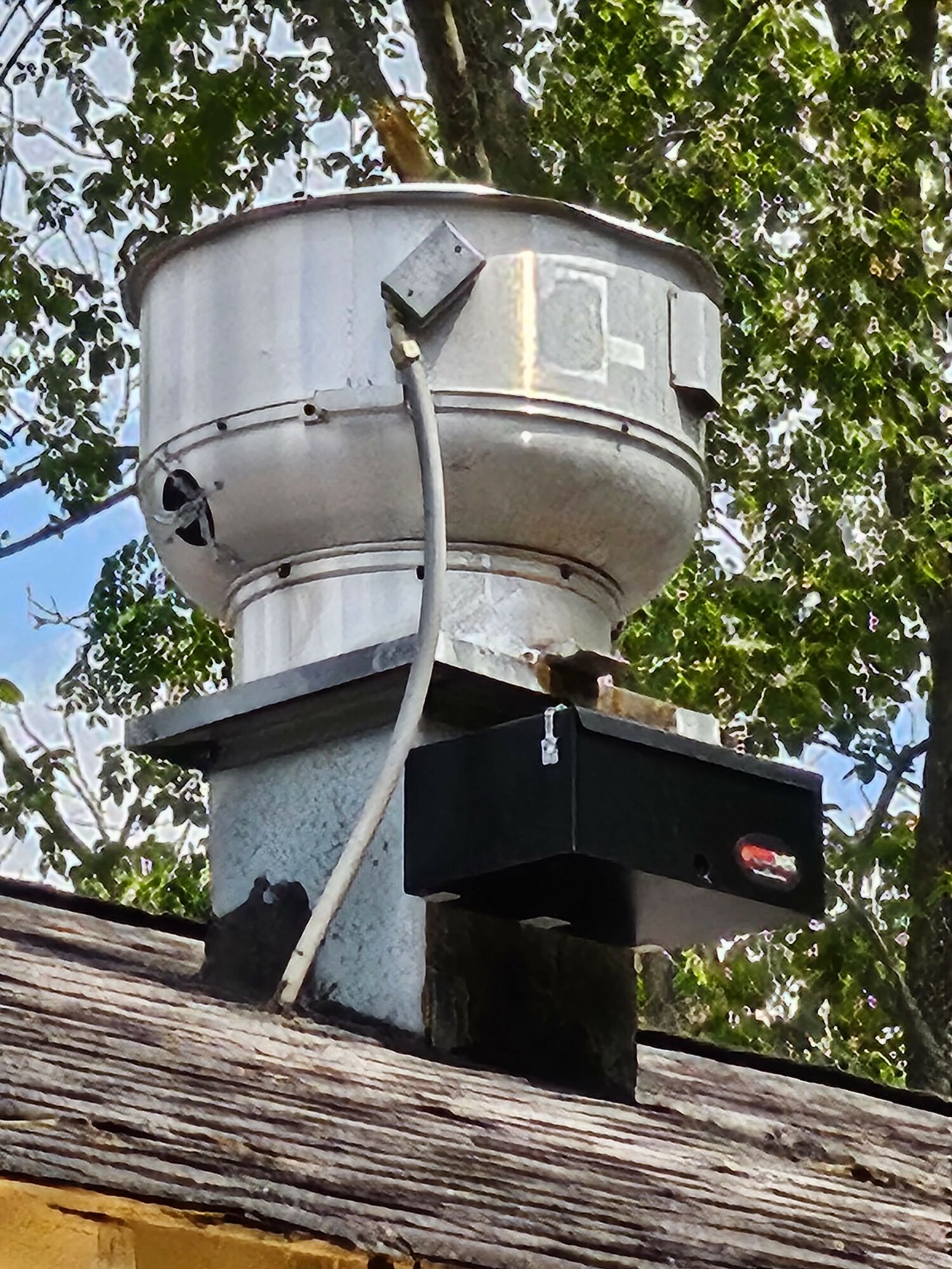 Metal cylindrical device mounted on a wooden surface with trees in the background.