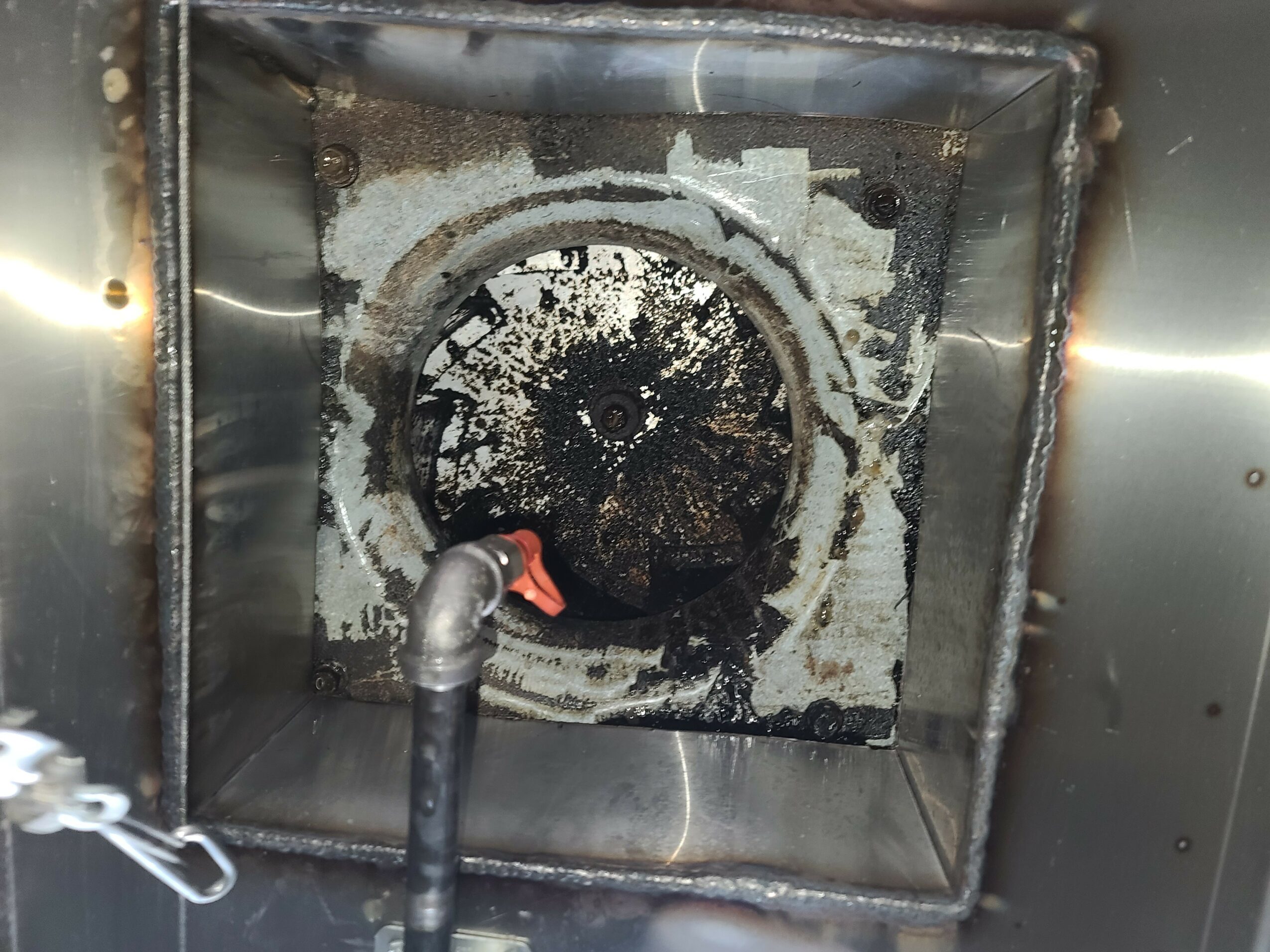 Interior of a metal machine with a circular, corroded, and burnt component, surrounded by a square metal frame.