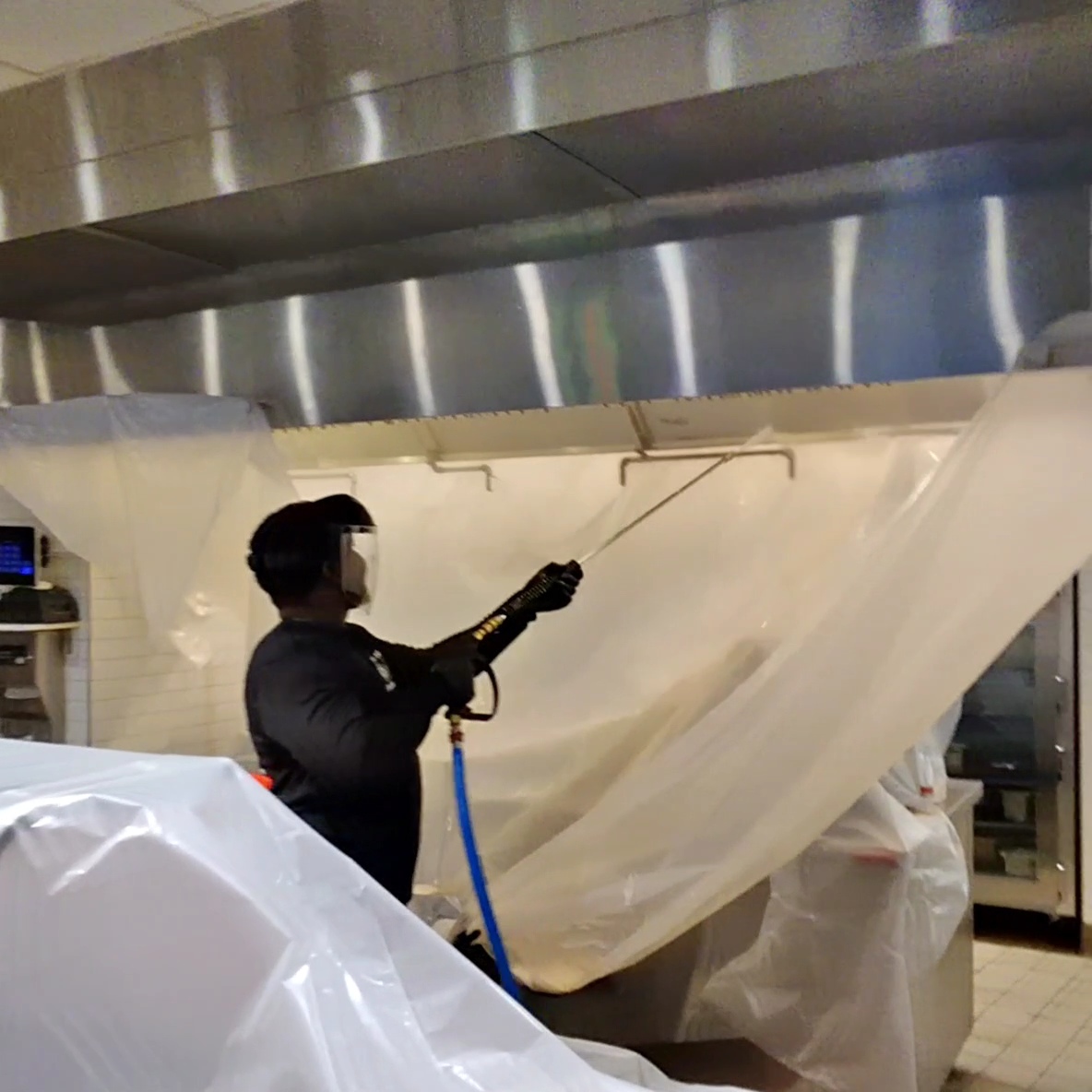 Person operating a machine with a large sheet of material in a kitchen or industrial setting.