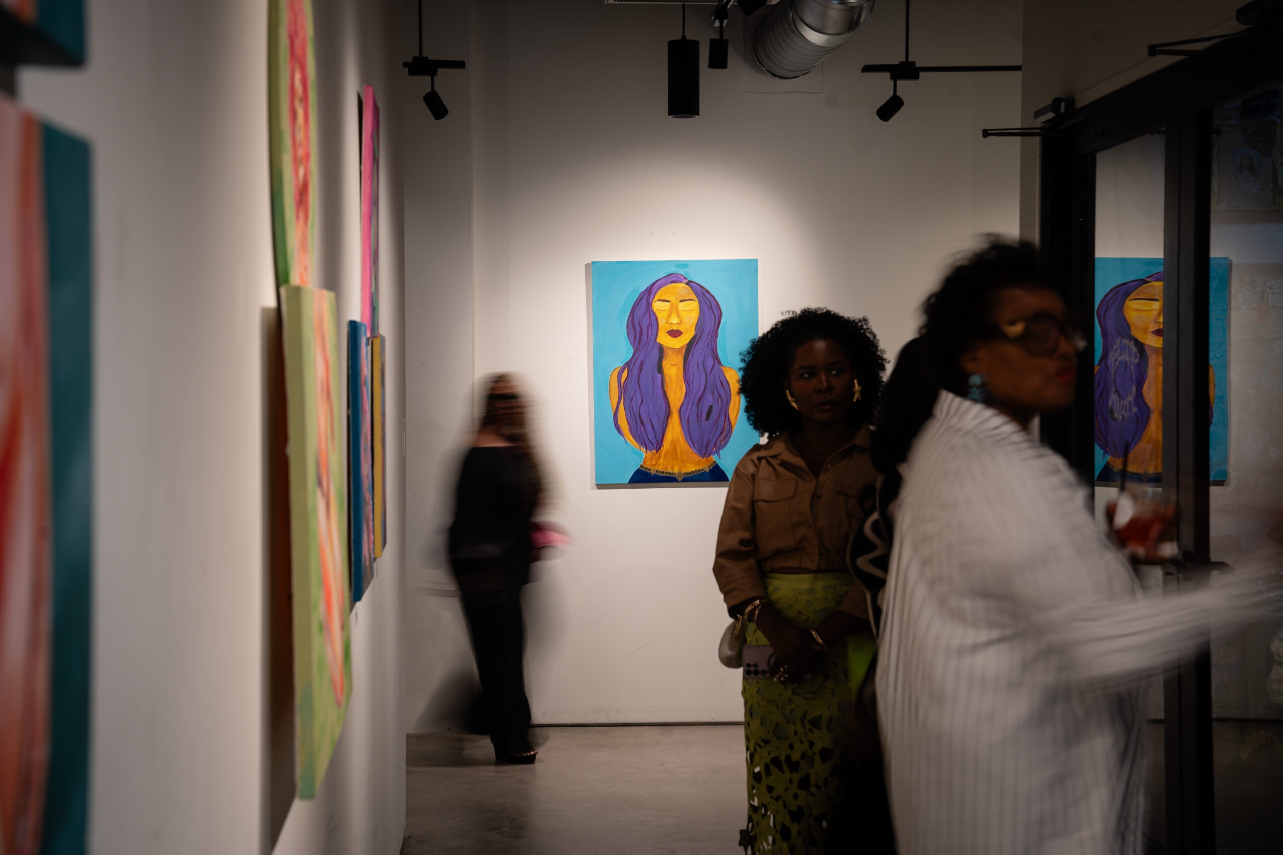 Gallery with colorful paintings, including a portrait of a woman with long hair, and people viewing art.