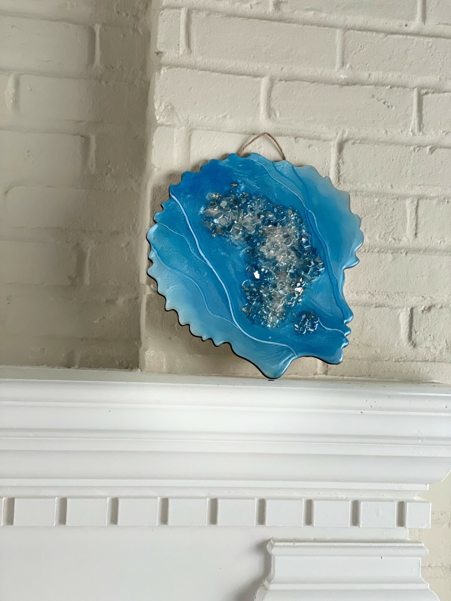 Decorative blue shell-shaped object with bubbles, hanging on a white brick wall, above a white shelf.