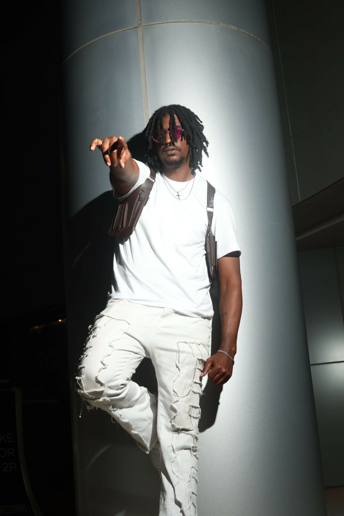 Person lying on a large, curved surface, wearing white clothing and a black scarf, holding a phone, dark background.