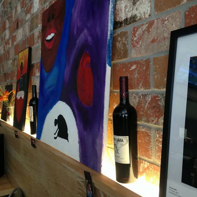 Shelf with paintings, a wine bottle, and a framed picture against a brick wall.