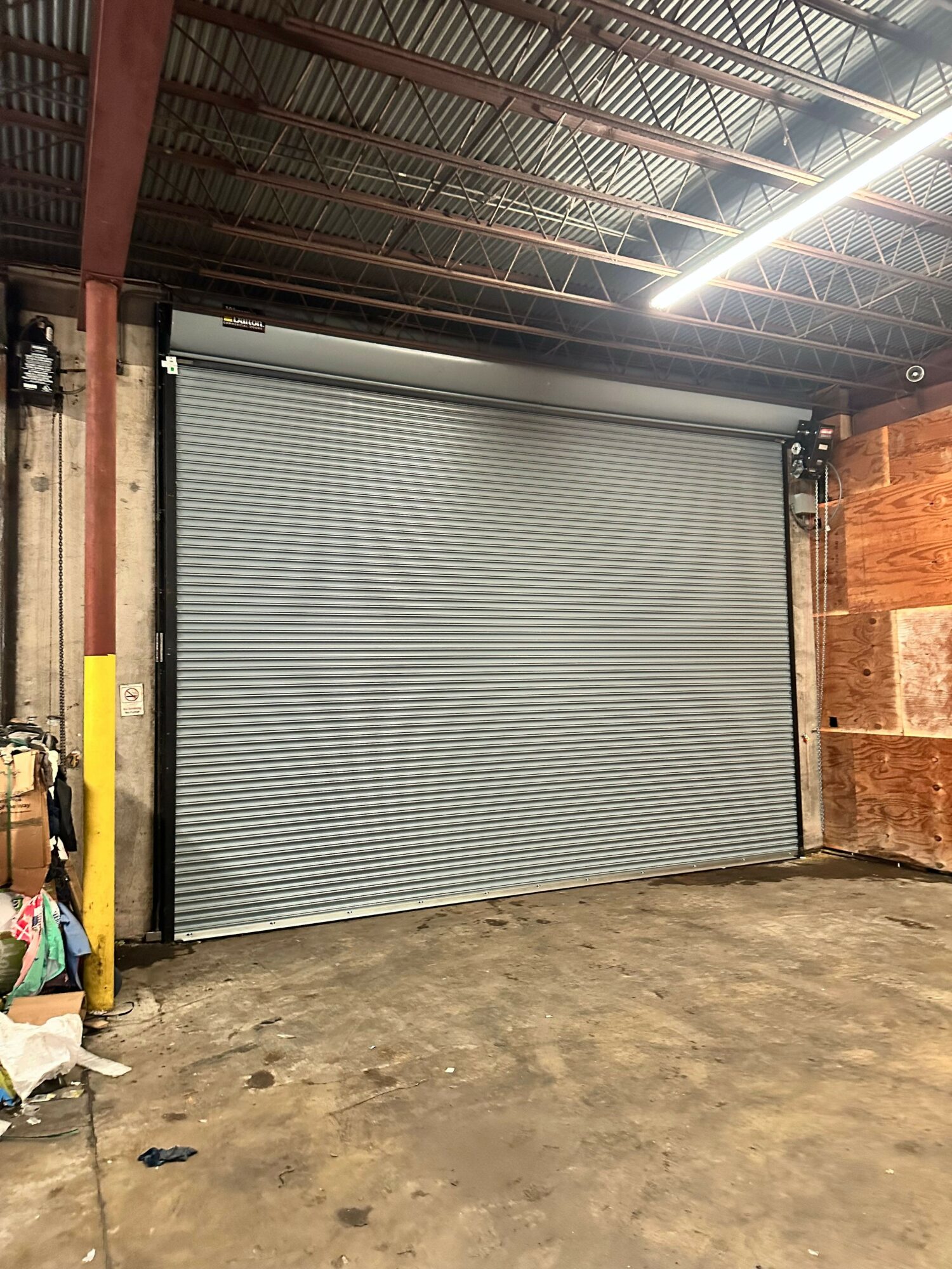 Closed metal roll-up door in a garage with concrete floor and wooden wall in background.