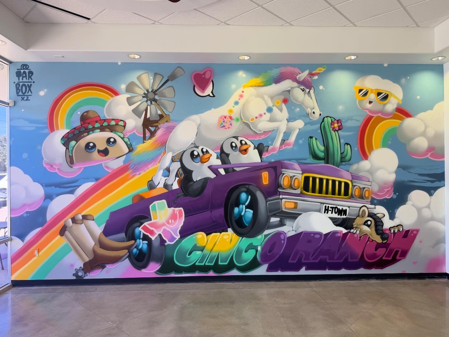 Colorful mural with cartoon animals, rainbow, unicorn, panda, and a purple car, featuring vibrant clouds and playful elements.
