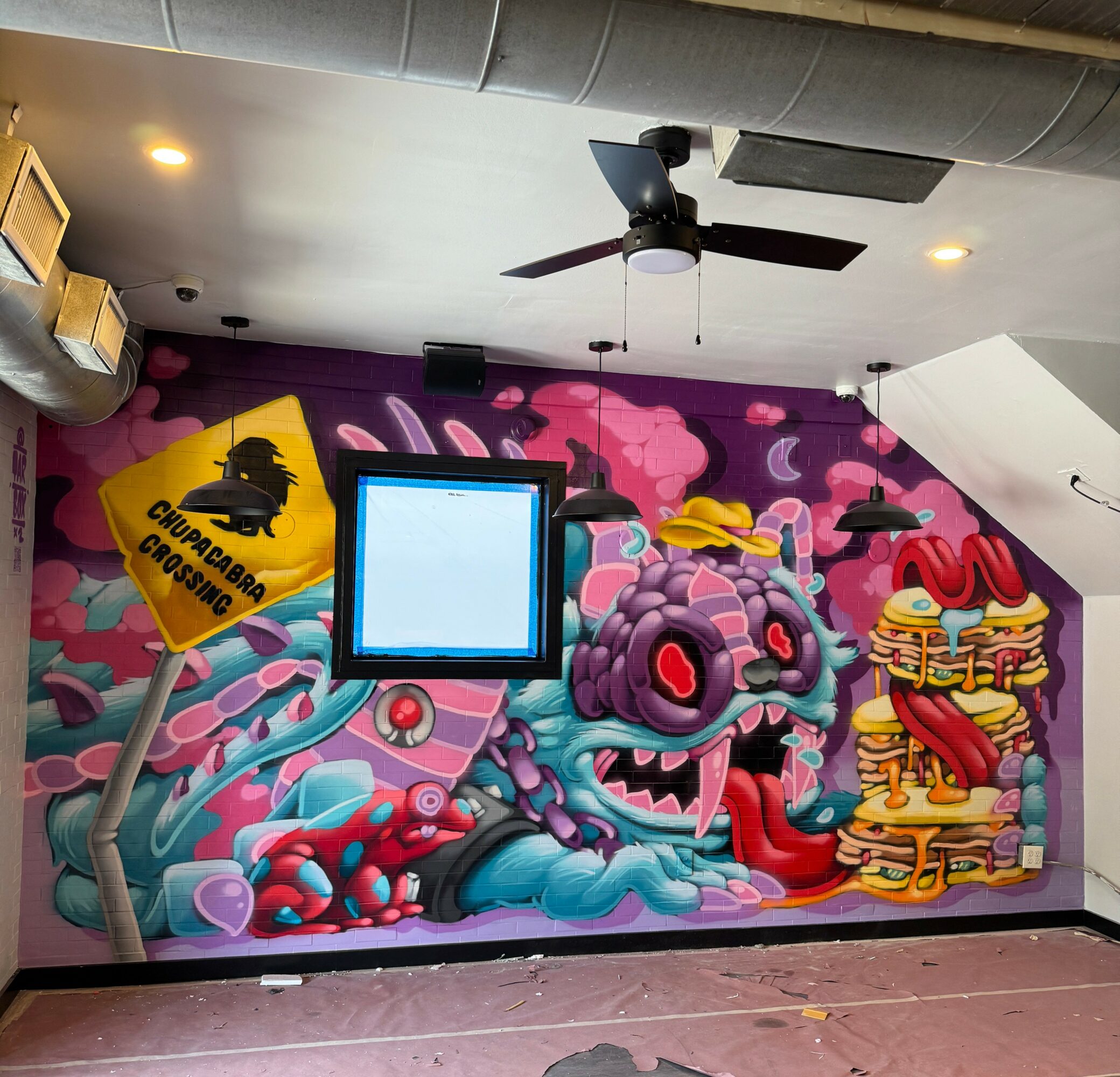 Colorful mural of a blue dragon with pink accents, a yellow sign, and a stack of pancakes on a pink background.
