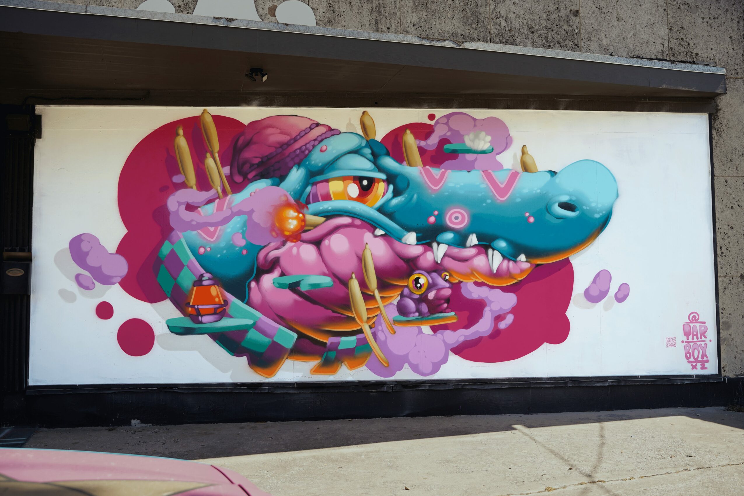 Colorful graffiti of a cartoonish blue crocodile with pink and purple accents, surrounded by abstract shapes and clouds.