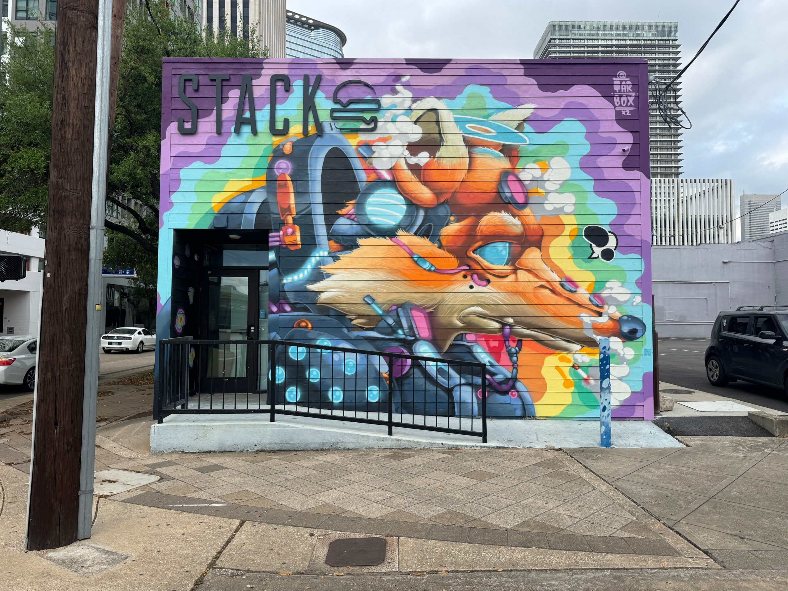 Colorful mural of a dog with rainbow background, the word 'JACK' at top left, on a purple wall.