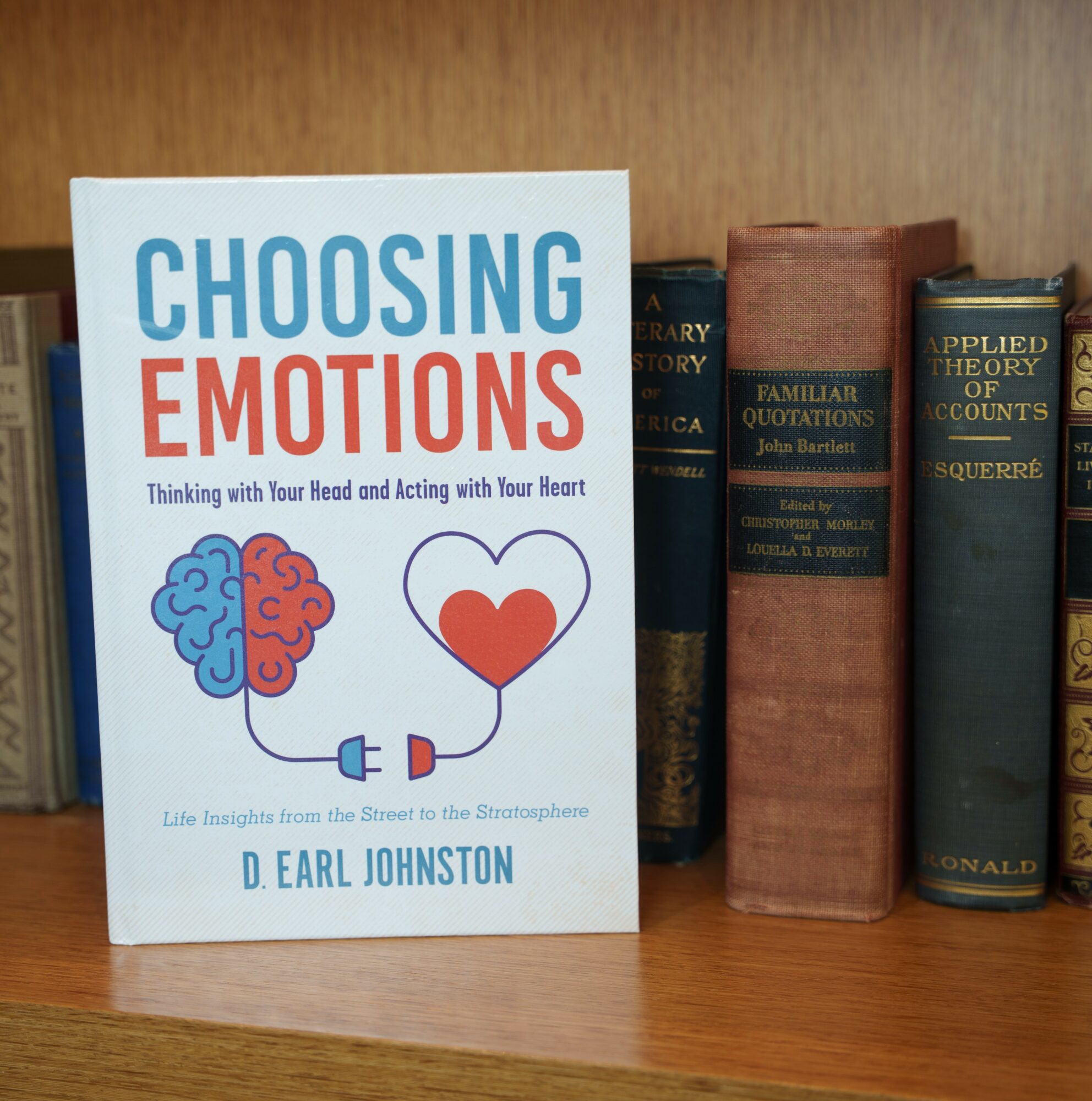 Book titled 'Choosing Emotions' with a brain and heart illustration on a wooden shelf, next to other books.