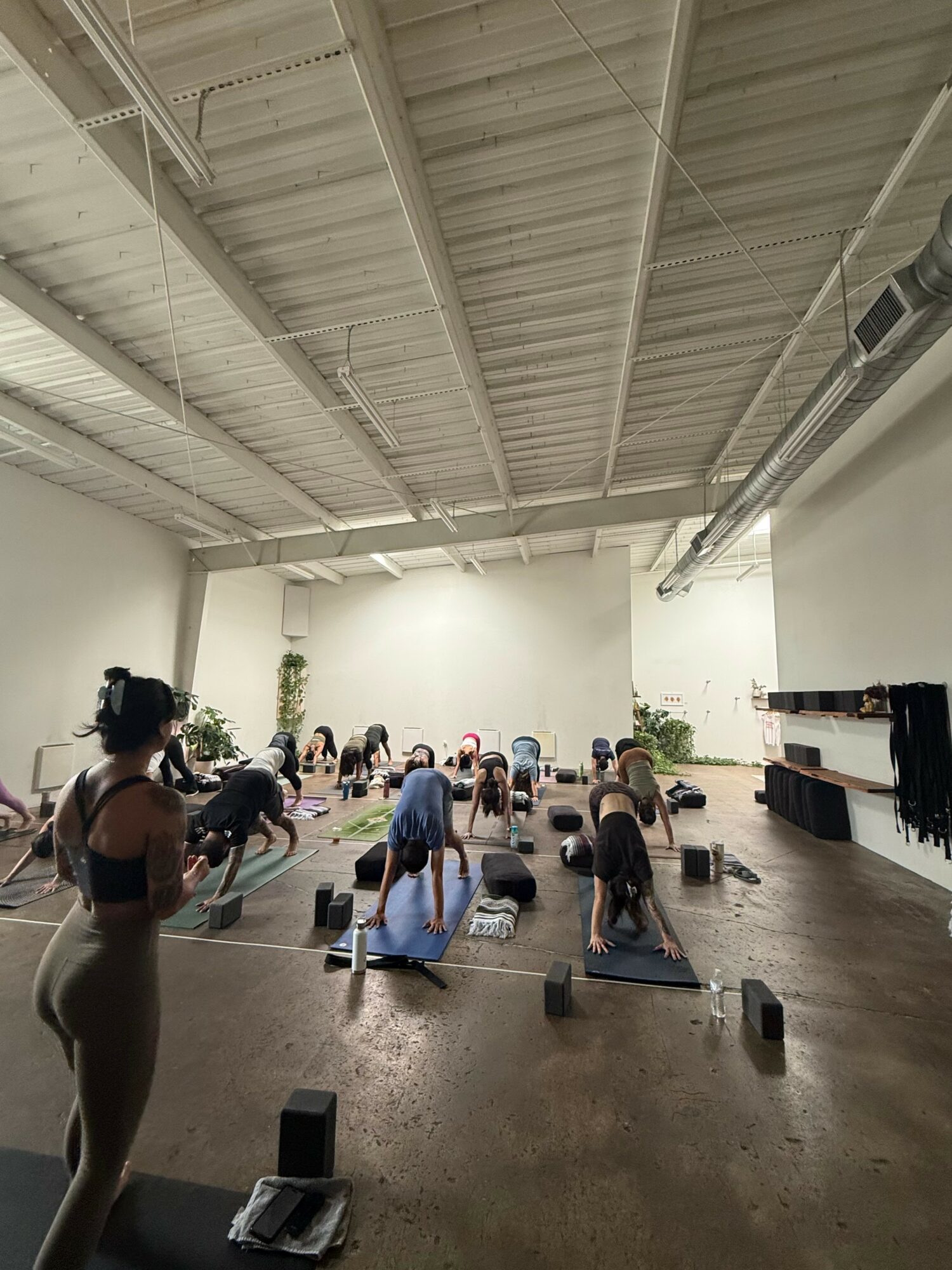 People participating in a yoga class in a spacious, industrial-style studio with high ceilings and minimal decor.