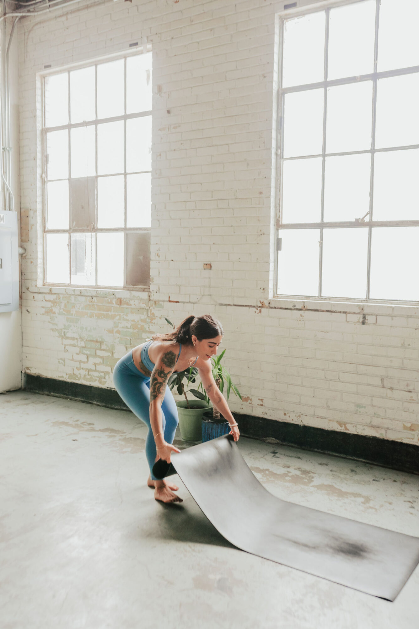 Person unrolling a large sheet of paper on the floor in a bright room with white brick walls and large windows.