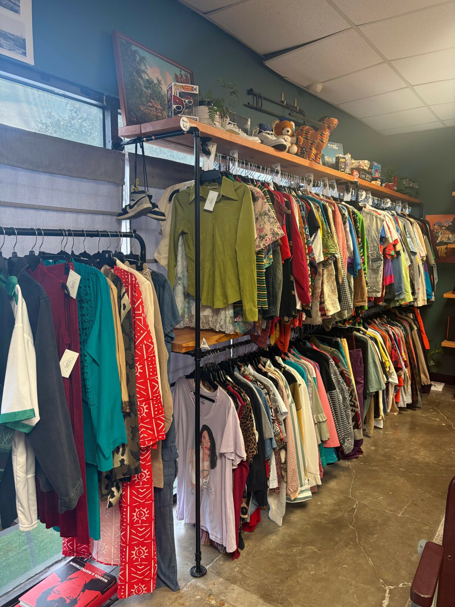 Clothing racks filled with various garments in a store, viewed from the side, with a ceiling and window visible.