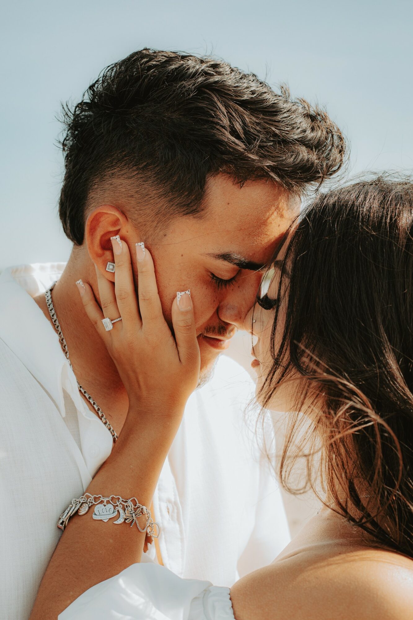 Two people with closed eyes touching foreheads and faces close together, one with hand on the other's face, smiling gently.