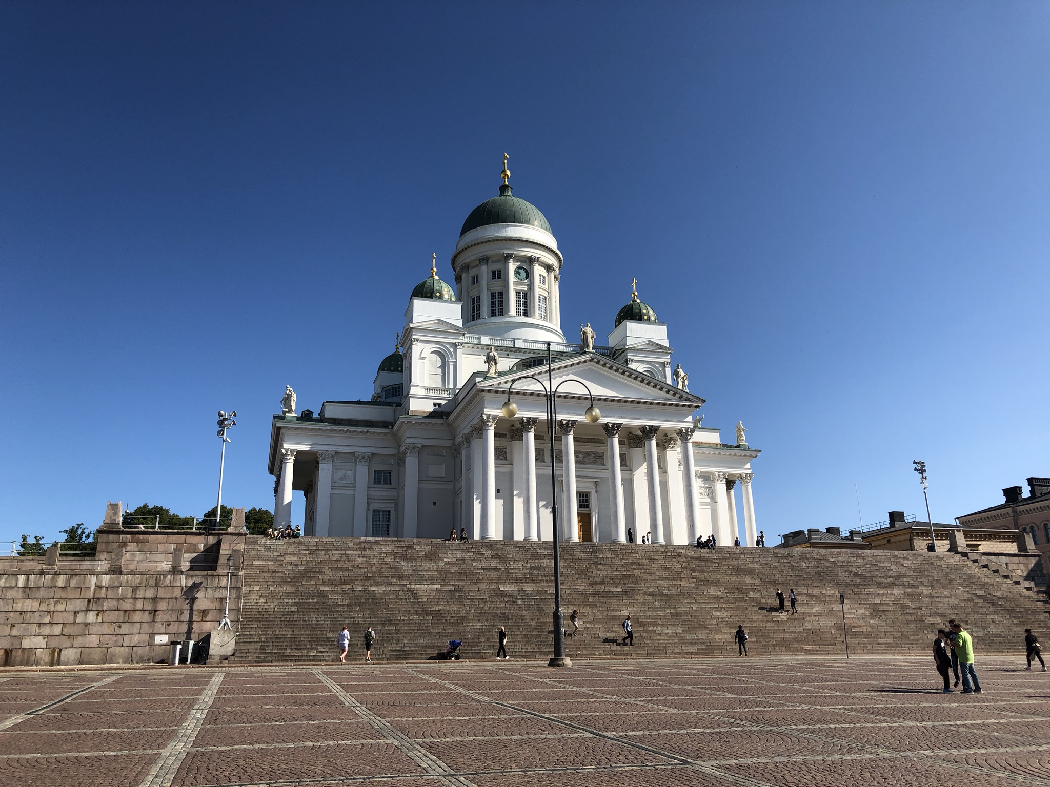 White church with domes and columns on a stepped platform under a clear blue sky.