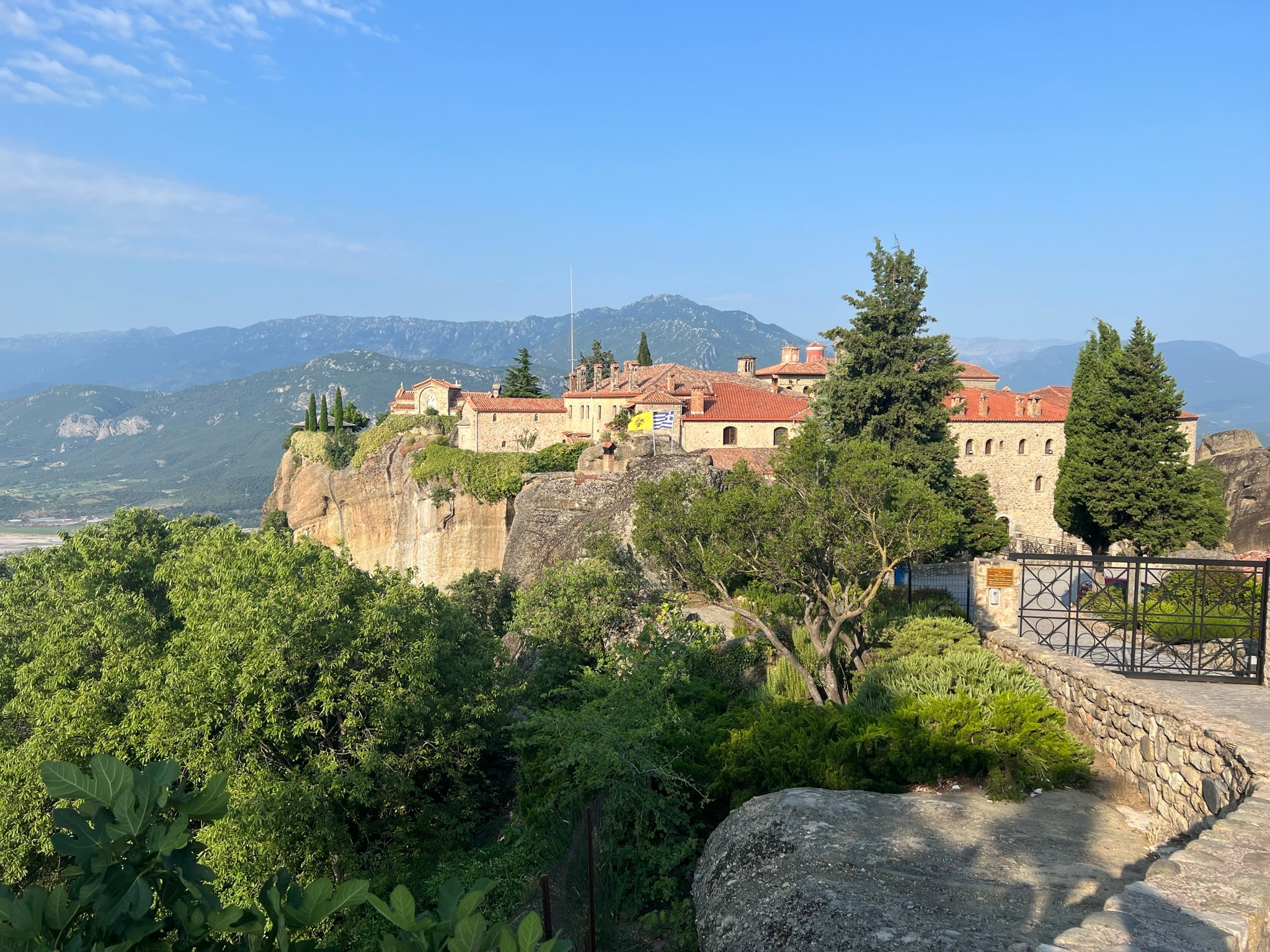 Castle on a hilltop with trees and mountains in the background, under a clear blue sky.
