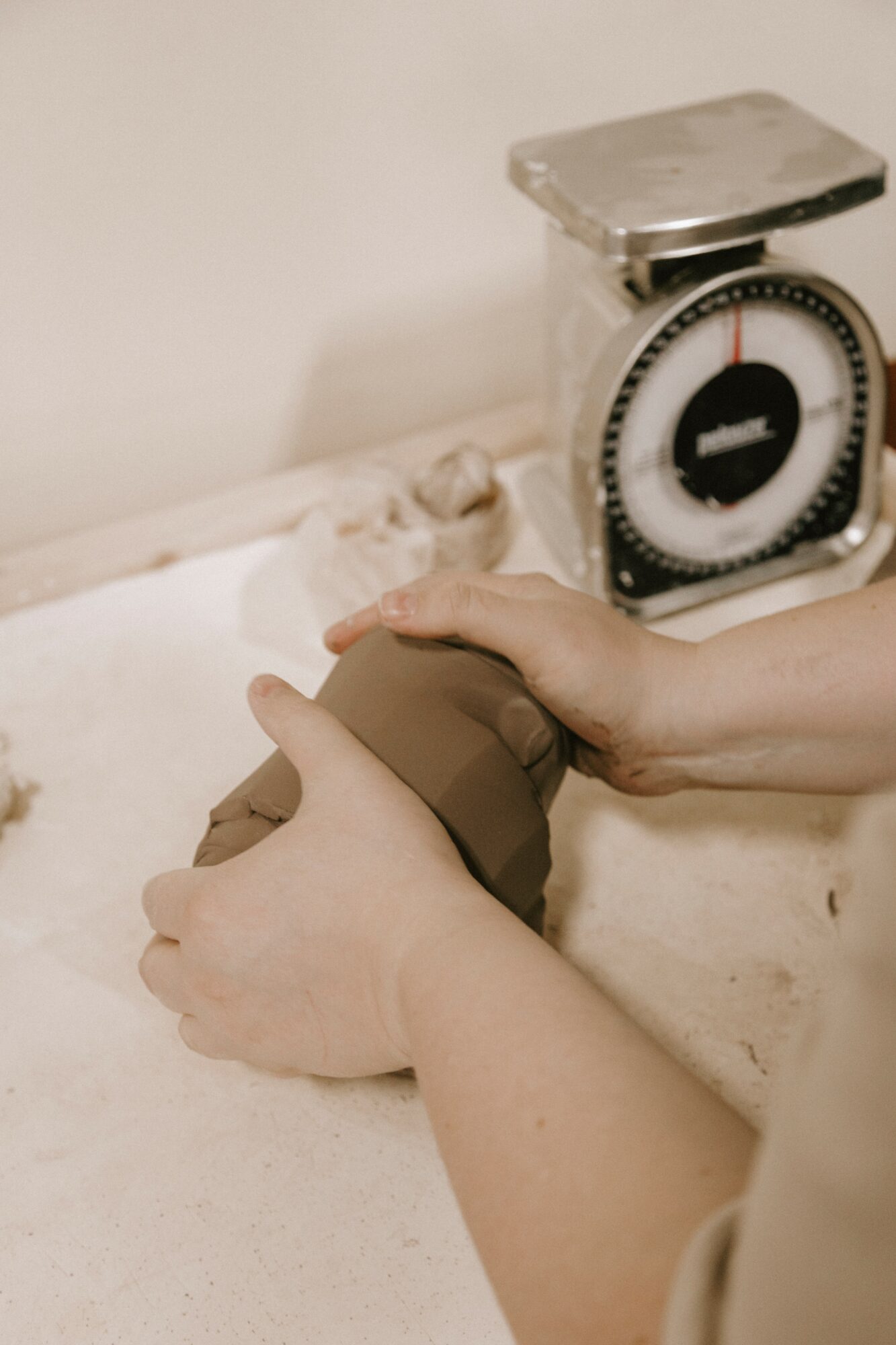 Person holding a baby's foot on a scale, with a weighing scale in the background, on a white surface.