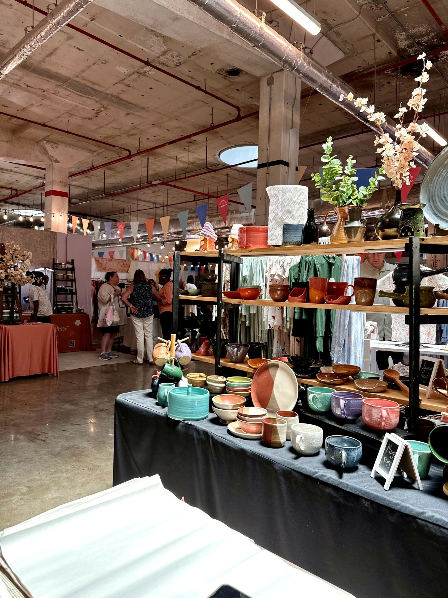 Display of colorful bowls and dishes on a black table at an indoor market or store, with people and other stalls in background.