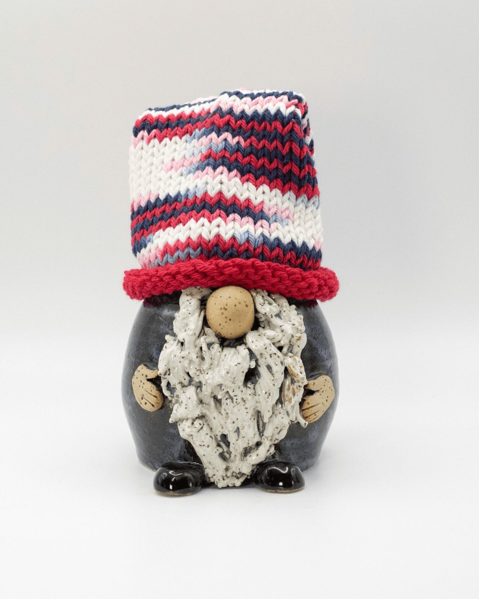 Small figurine with a colorful knitted hat, a textured face, and round wooden hands and feet, standing against a plain background.