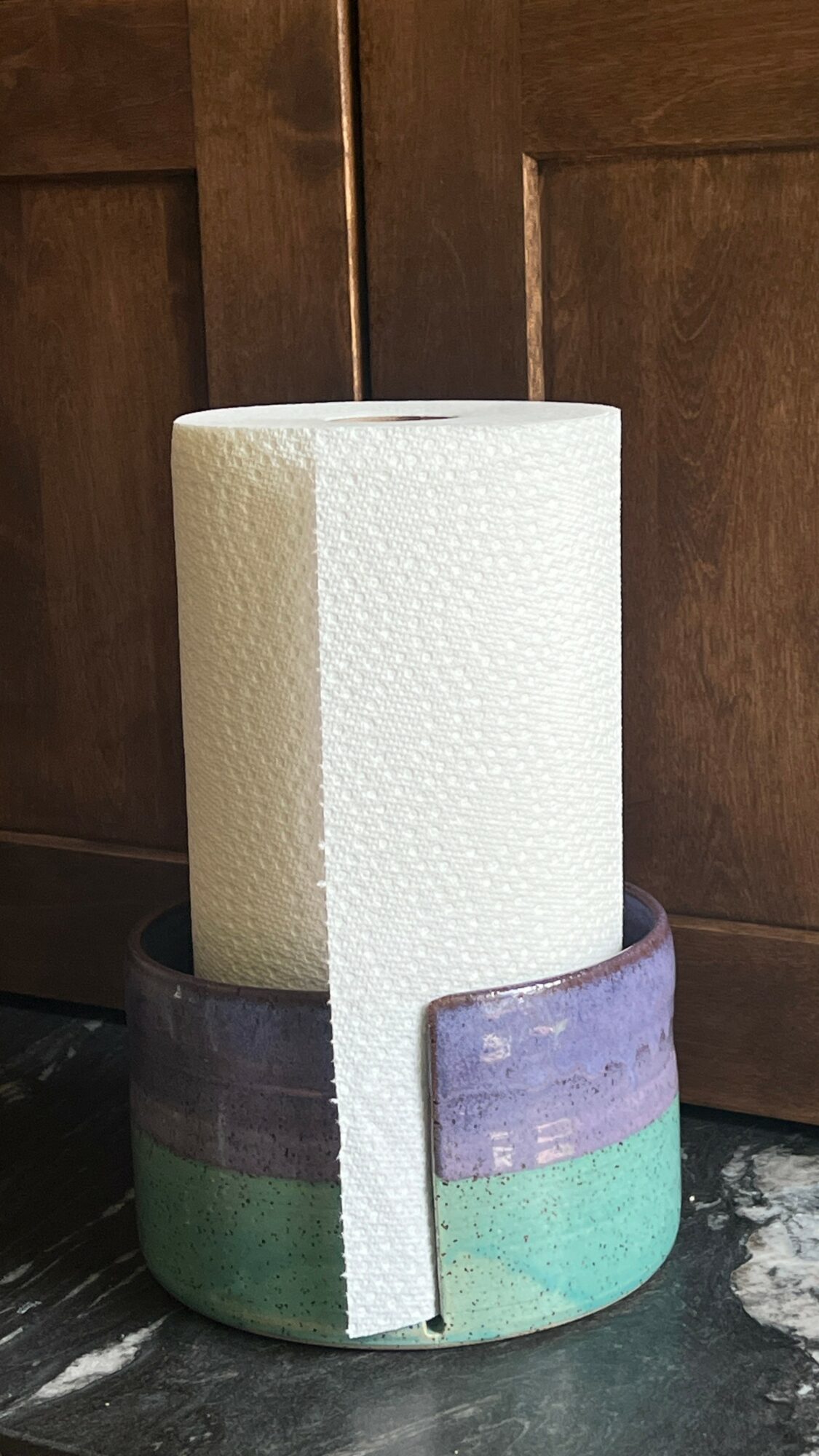 A roll of white paper towel in a multicolored holder on a dark surface with wooden background.