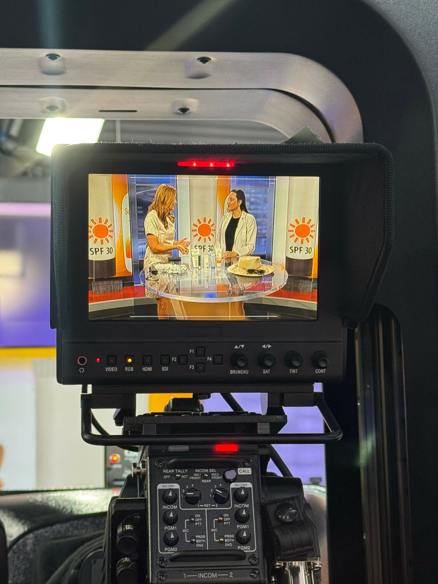 Camera monitor displaying a person in front of a backdrop with sun symbols, with camera equipment visible on the right.