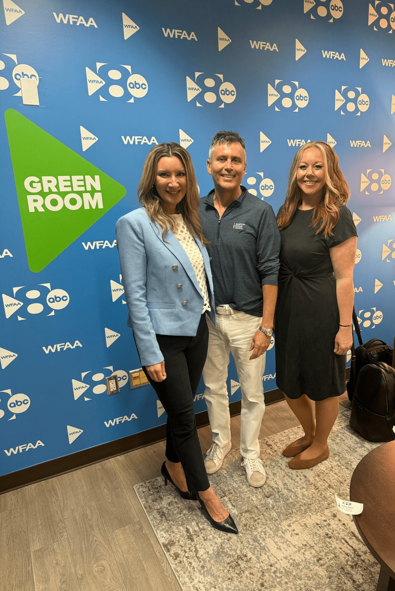 Three people standing together in front of a blue backdrop with logos, smiling for the photo.