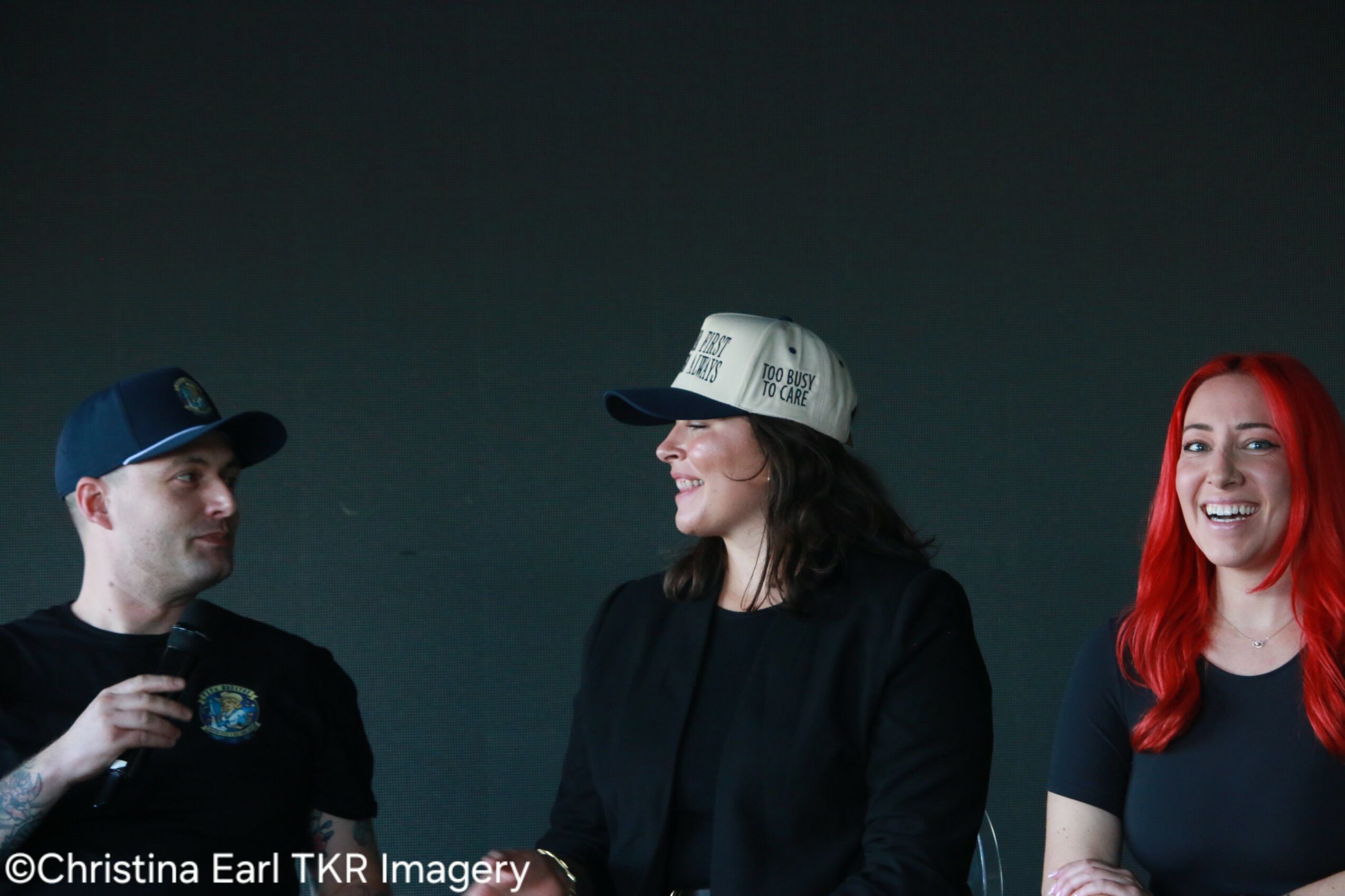 Three people smiling and talking, one with red hair, against a dark background.