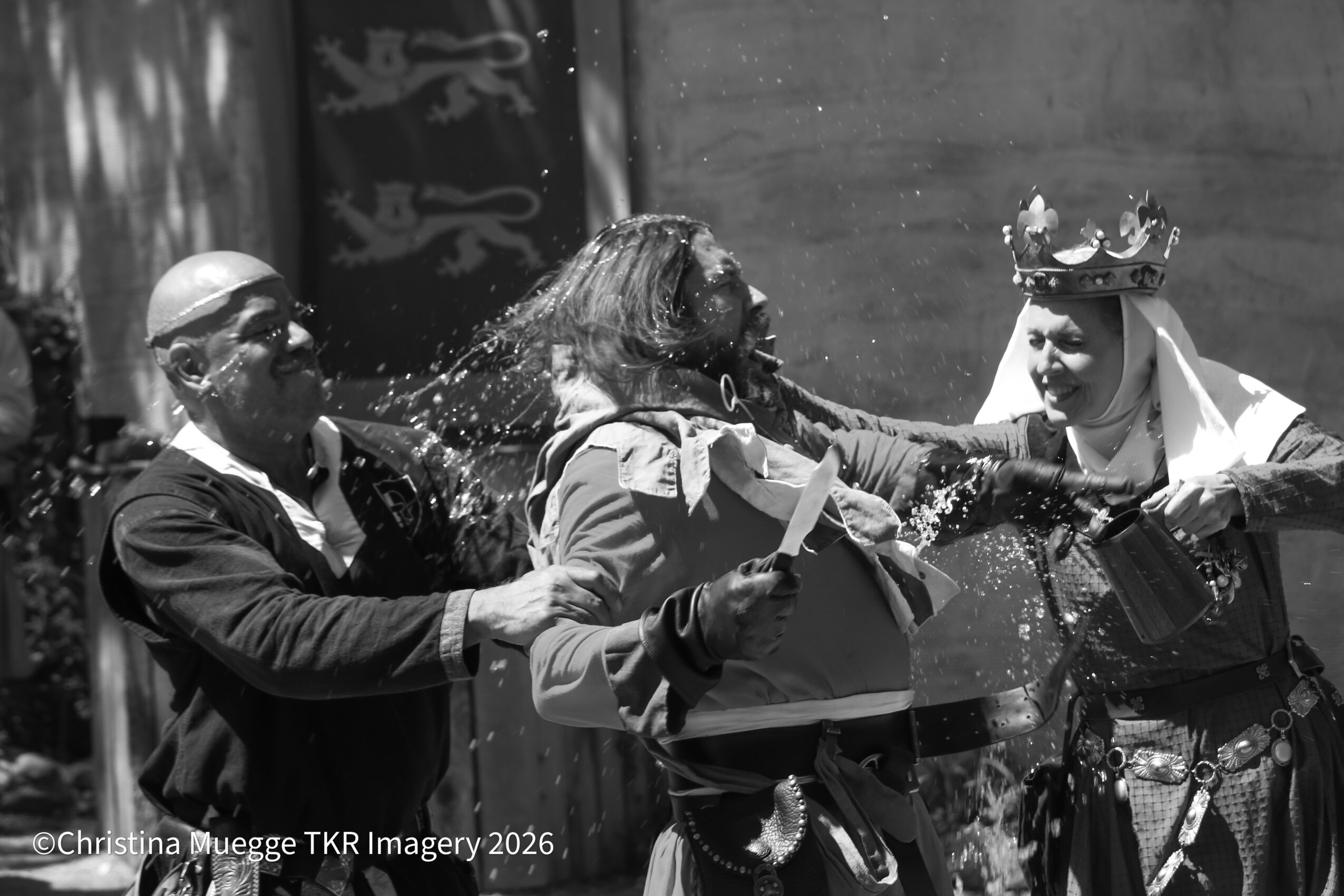 Three people participating in a water splash event outdoors, with one person wearing a crown and traditional clothing.