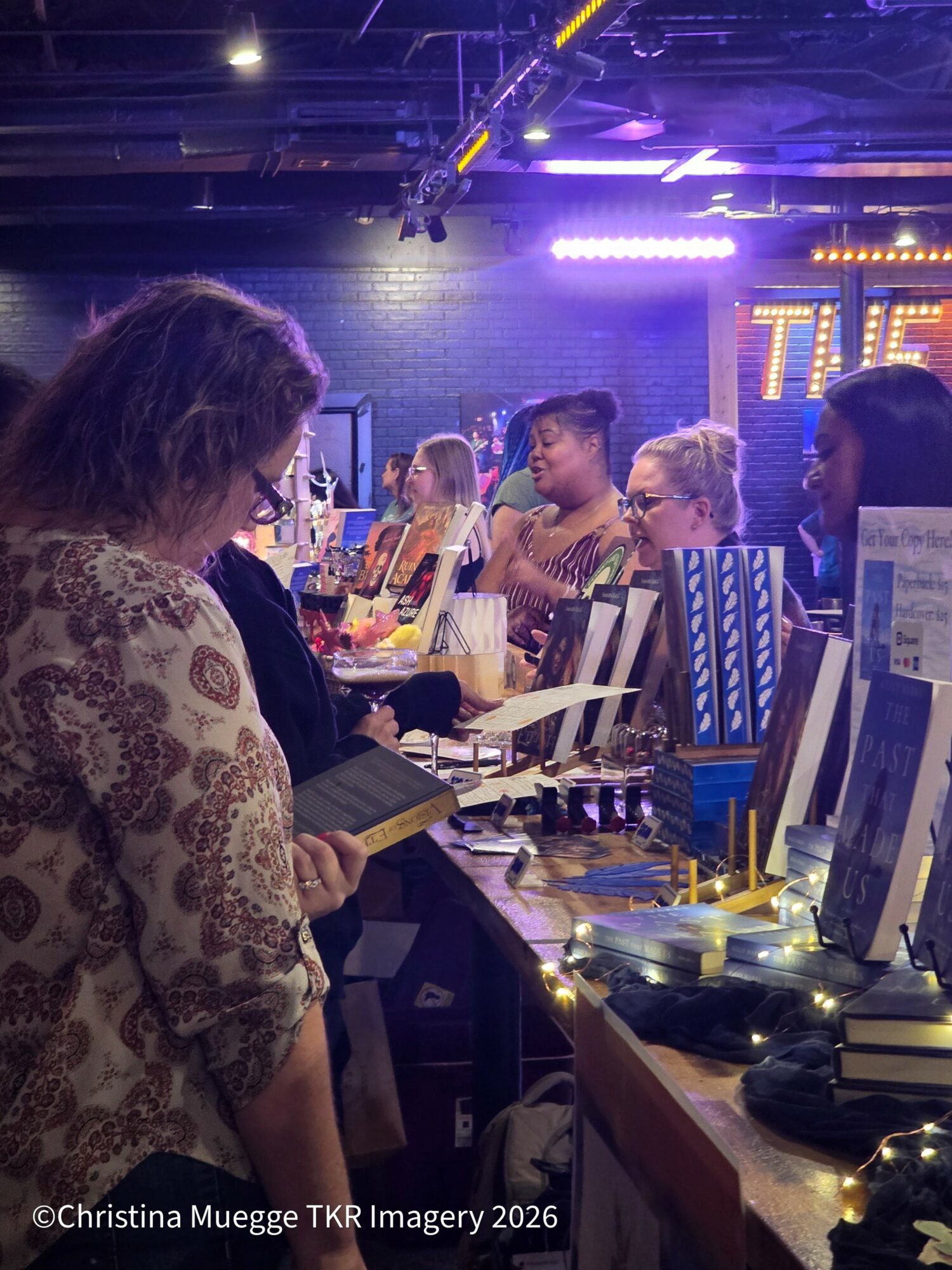 People browsing items at a market stall with colorful lights and displays, some looking at products and others talking.