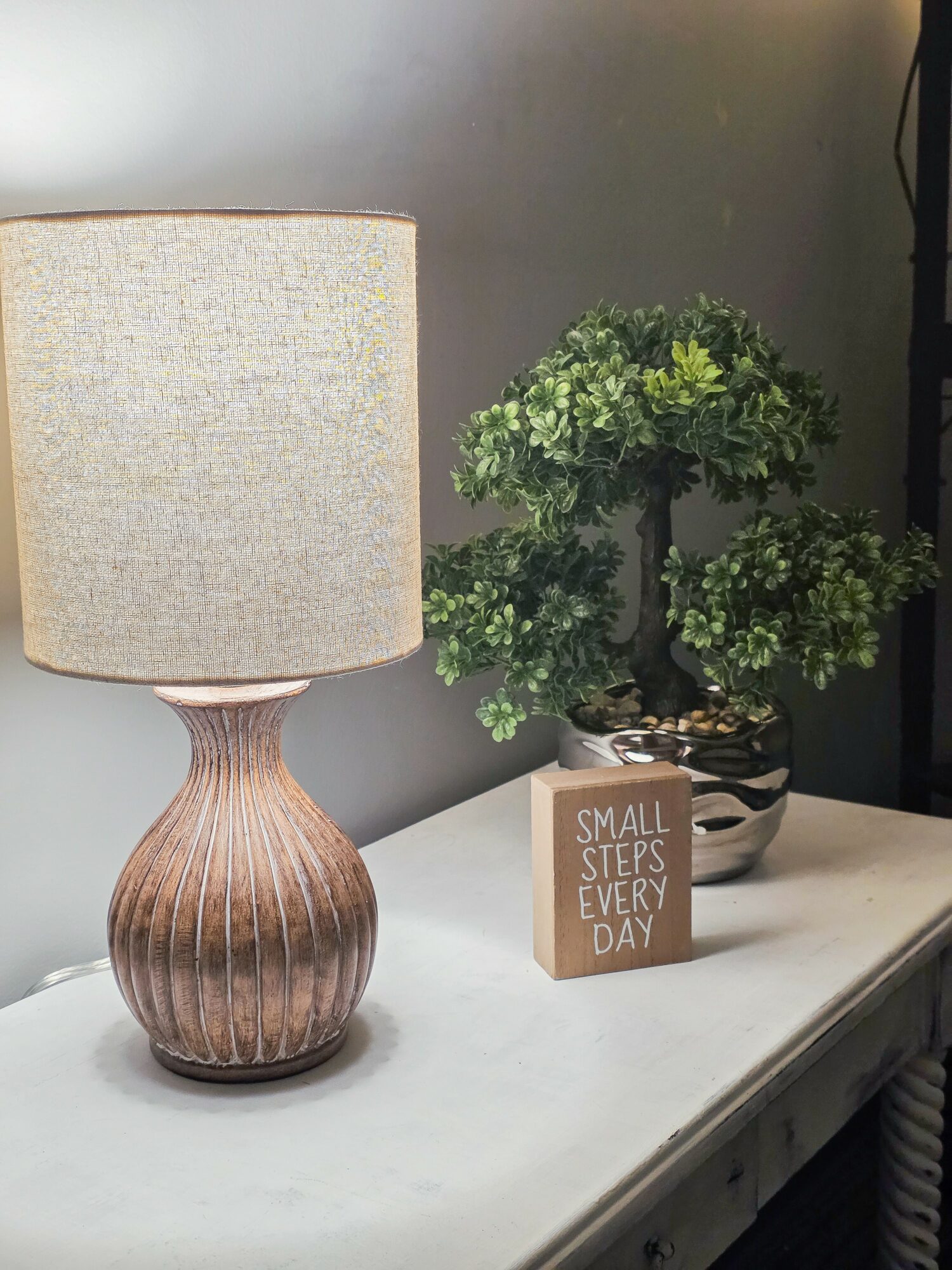 Table with a lamp, potted plant, and small sign reading 'Small Steps Every Day'.
