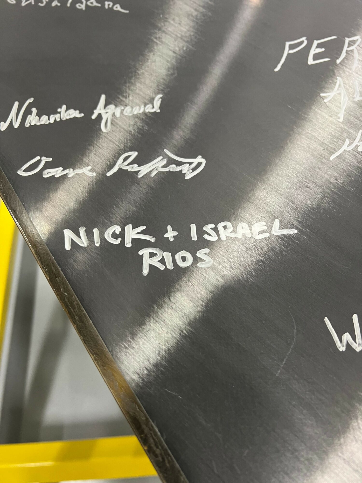 Close-up of a metallic surface with handwritten white text, including names and phrases.