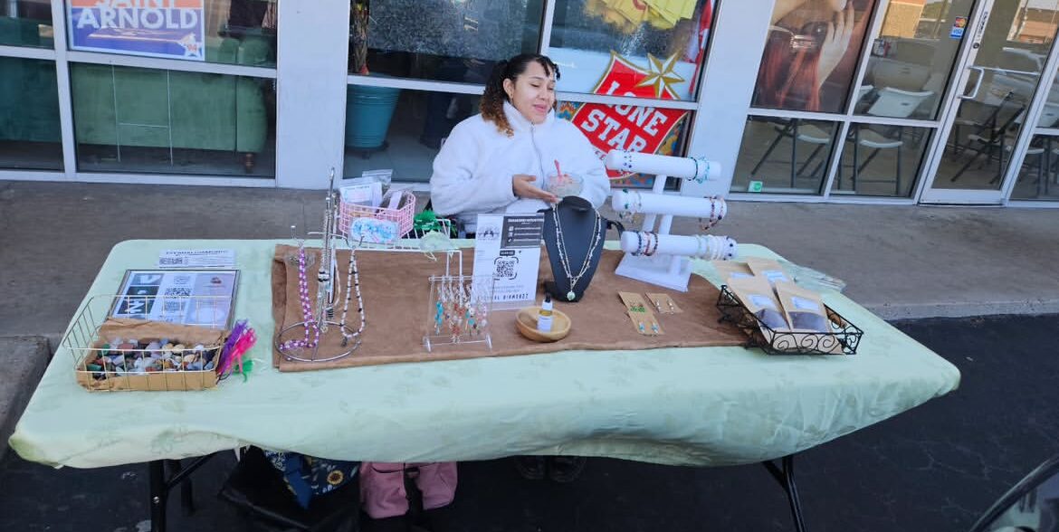 Person sitting behind a table with jewelry and accessories outside store, with a