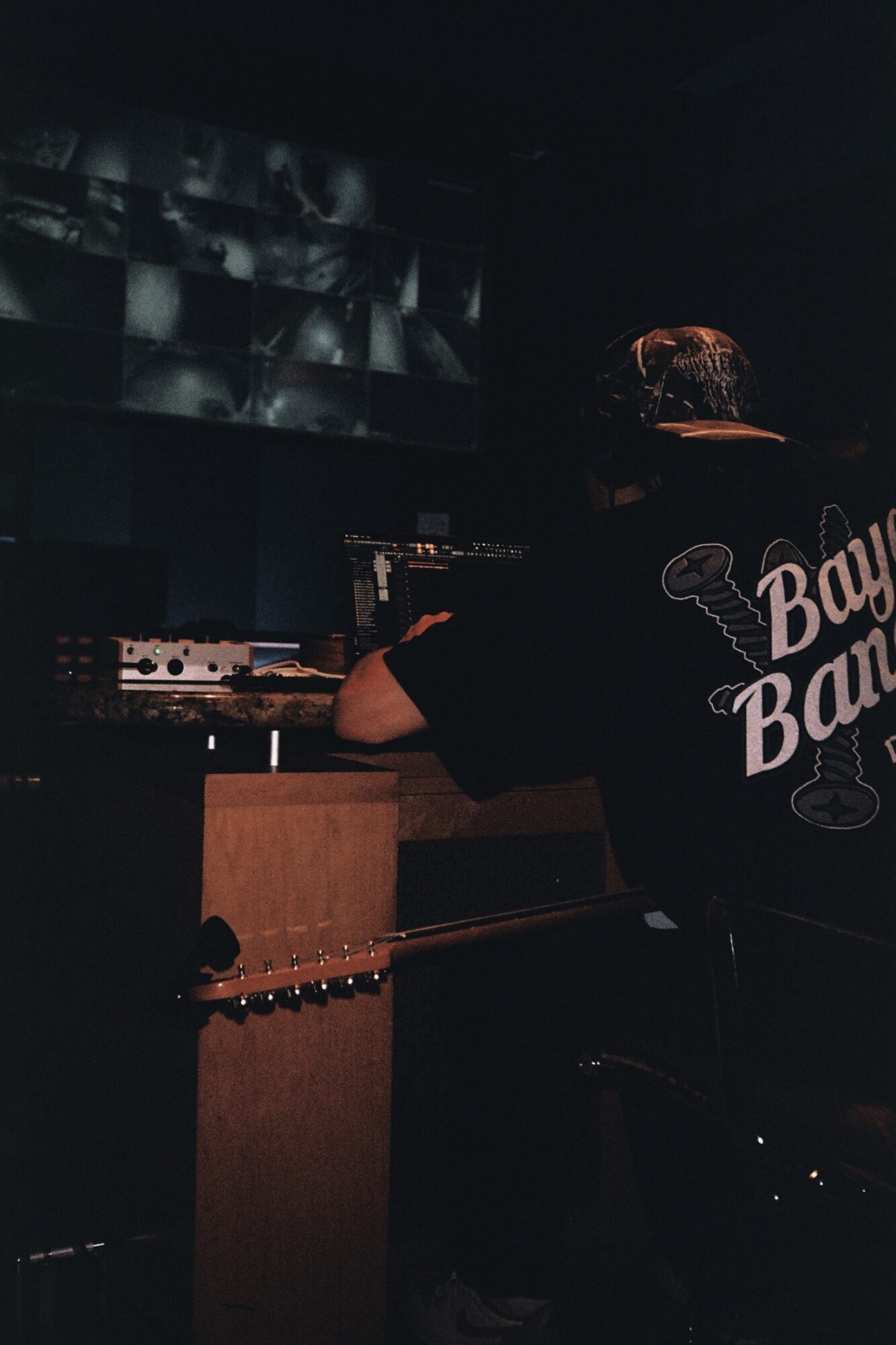 Person with short hair wearing a black shirt with white text, working with electronic equipment in a dark room.