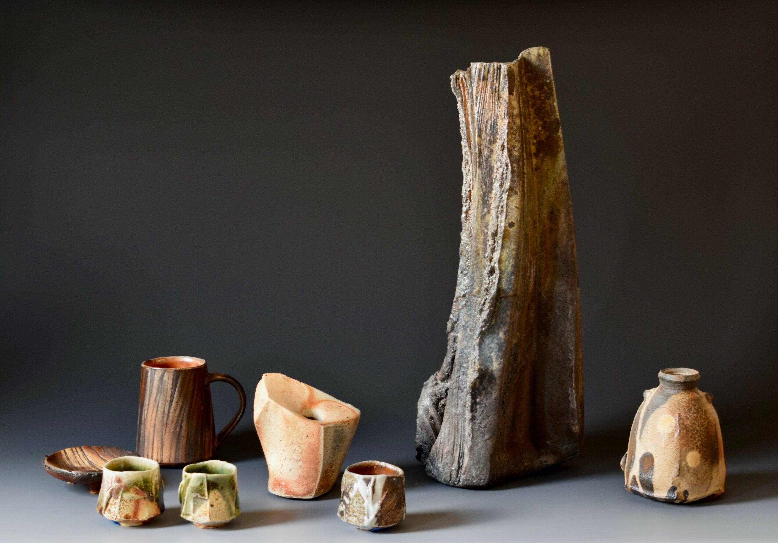 Collection of pottery and a tall, textured stone on a dark background.