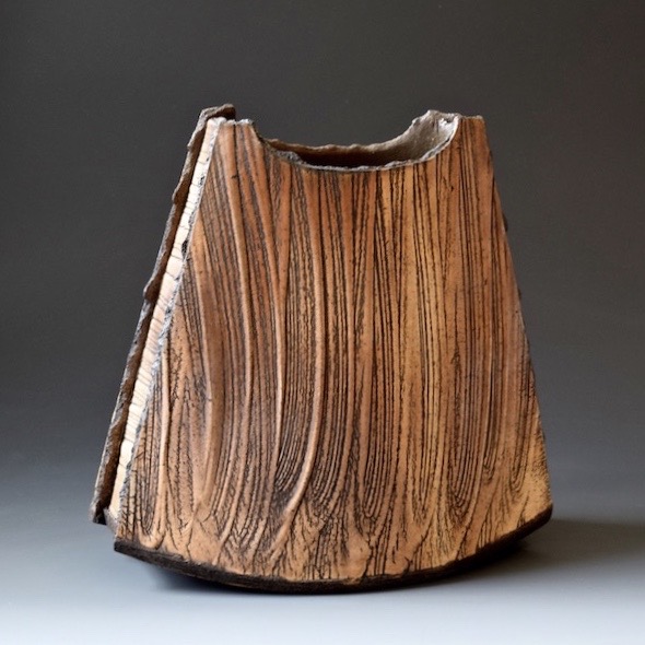 A wooden object with a curved top and vertical grain pattern, set against a dark background.