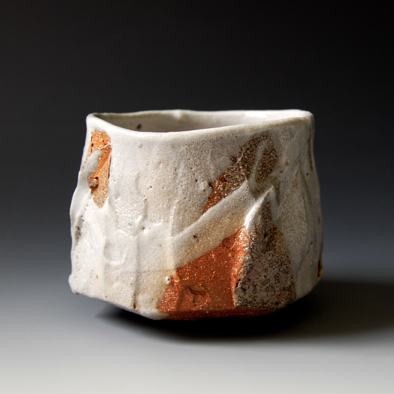 Ceramic cup with a textured surface and abstract reddish-brown and white glaze, set against a dark background.