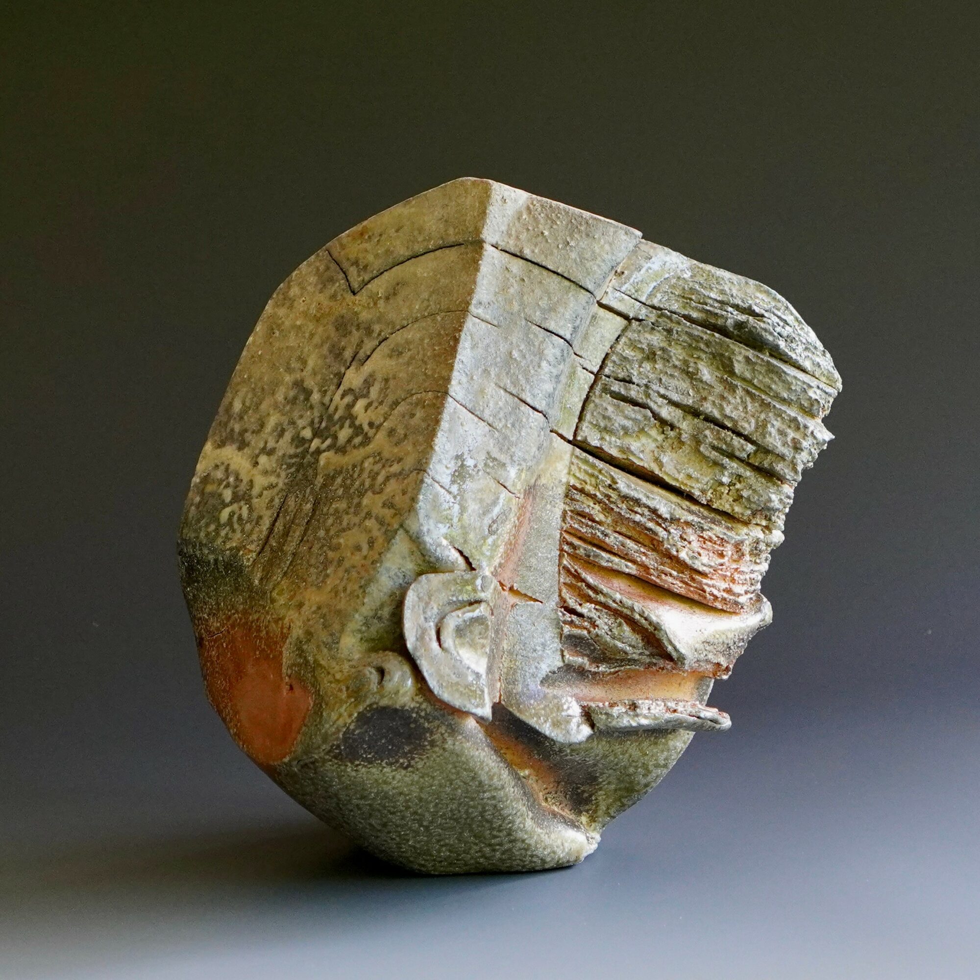 Fragmented ancient artifact with carved details, weathered surface, and layered textures, displayed against a dark background.