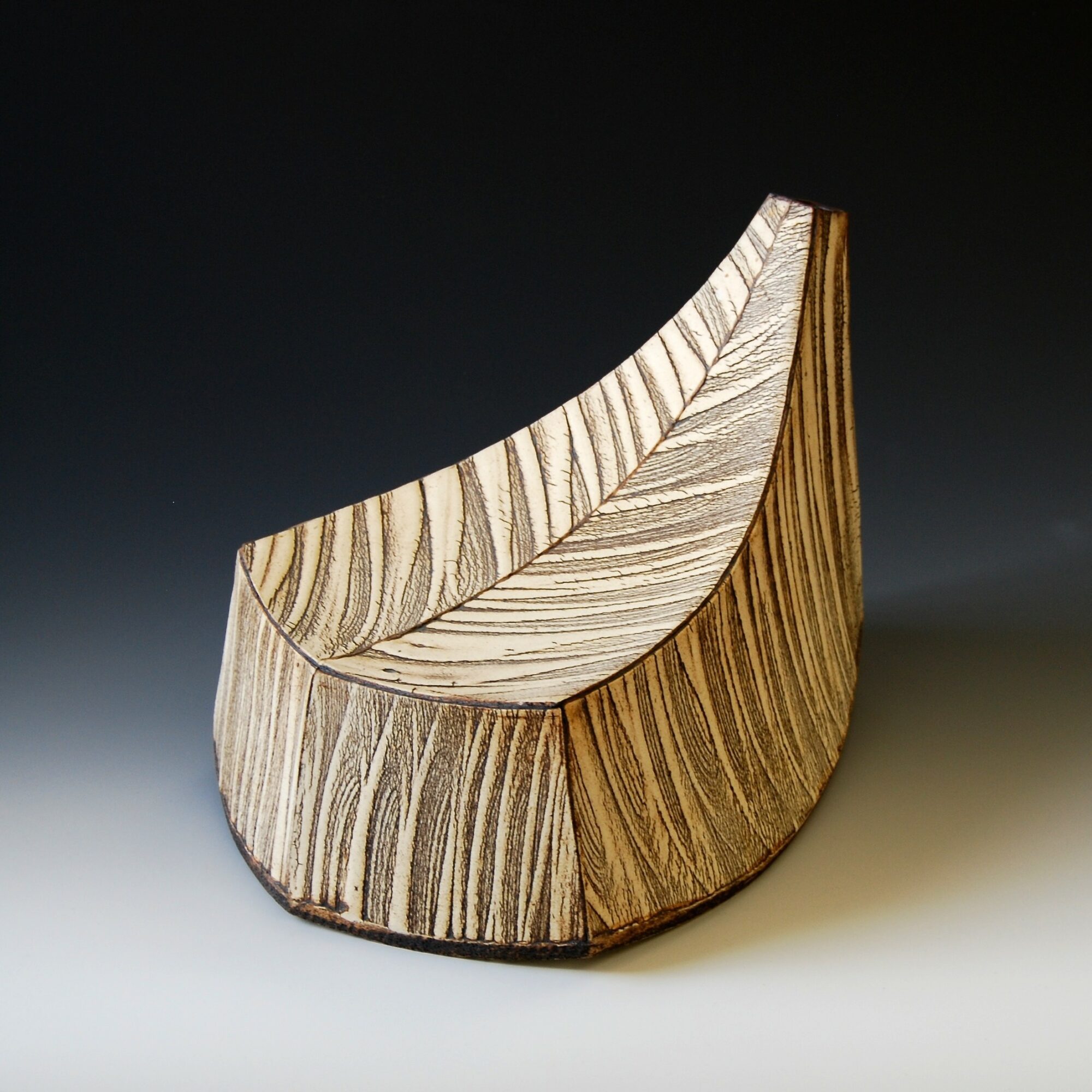 Wooden bowl with carved leaf pattern, curved shape, and natural wood grain, on a gradient background.