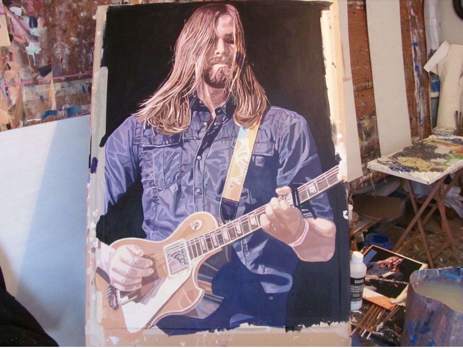 Painting of a person with long hair playing an electric guitar, wearing a blue shirt, on a black background.