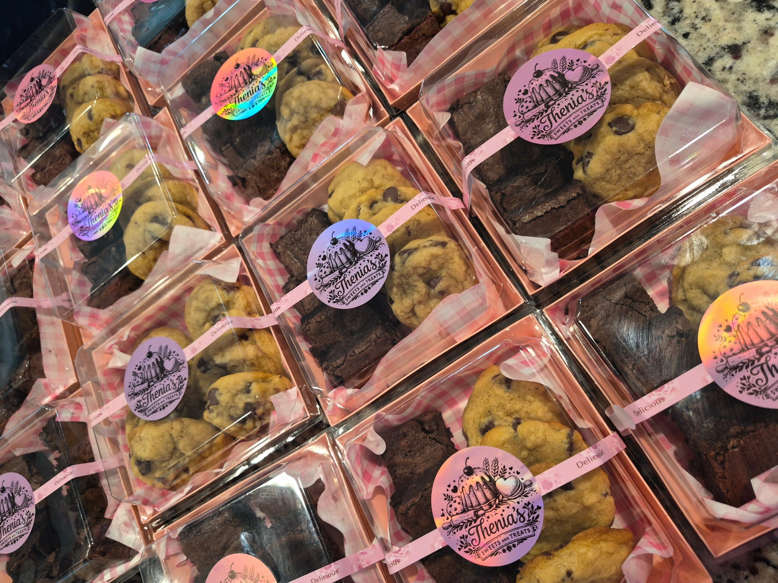 Multiple small clear plastic bags with cookies inside, pink labels, and pink sticks, arranged in a grid pattern.