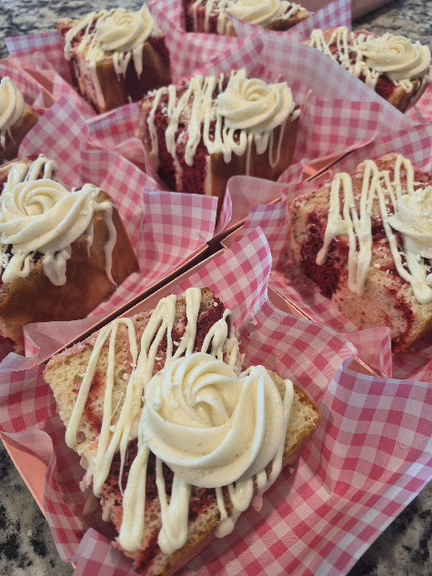 Cupcakes with white frosting and drizzle in pink checkered paper wrappers, arranged closely together.