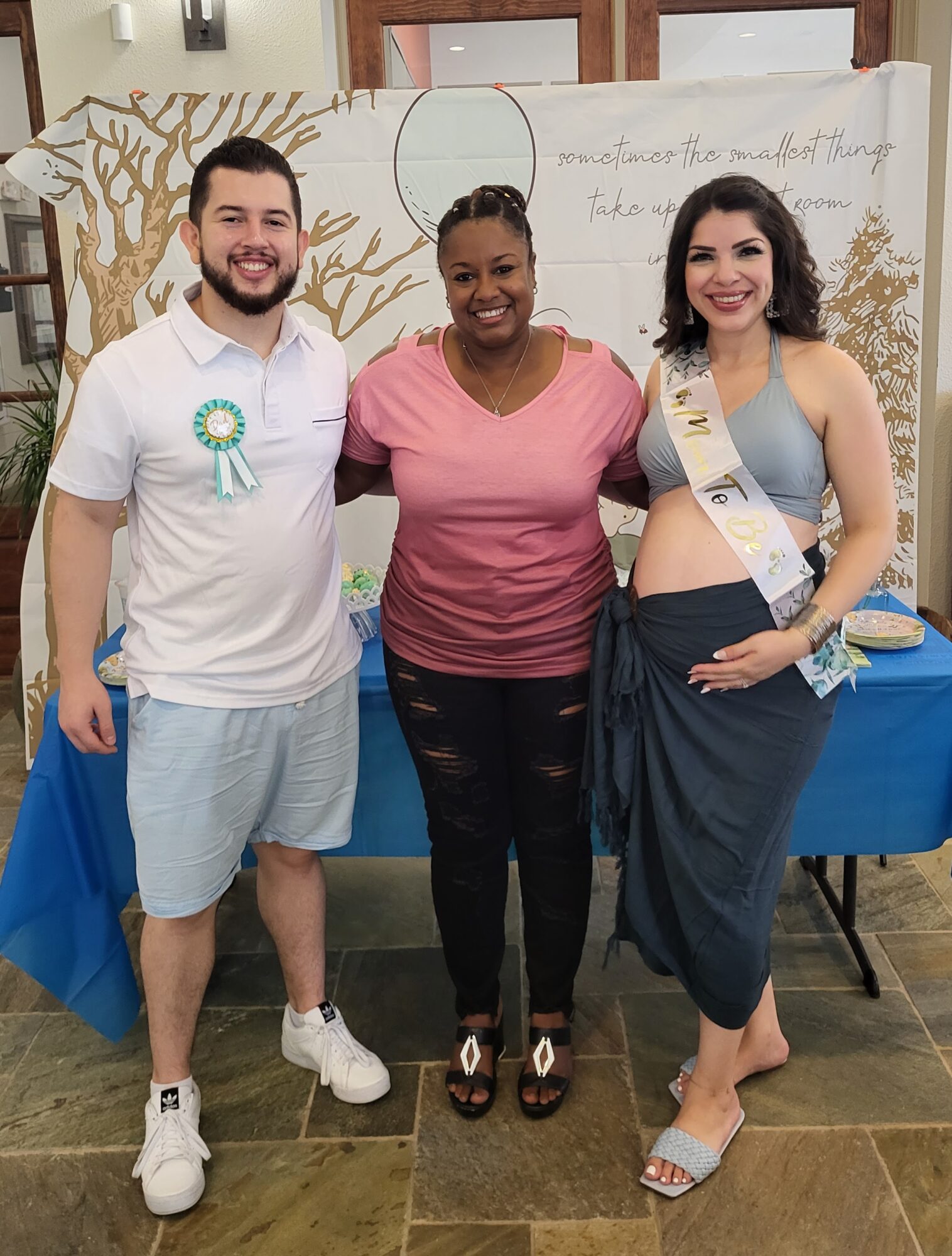 Three people standing together indoors, smiling, with a decorated backdrop and a table behind them.