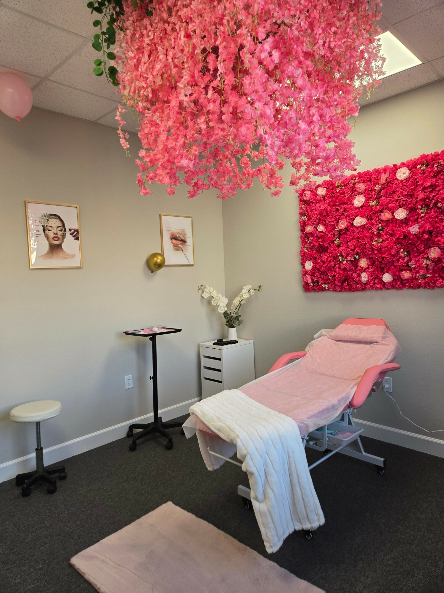 Room with pink flowering tree, pink and white furniture, and wall art, arranged in a cozy corner.