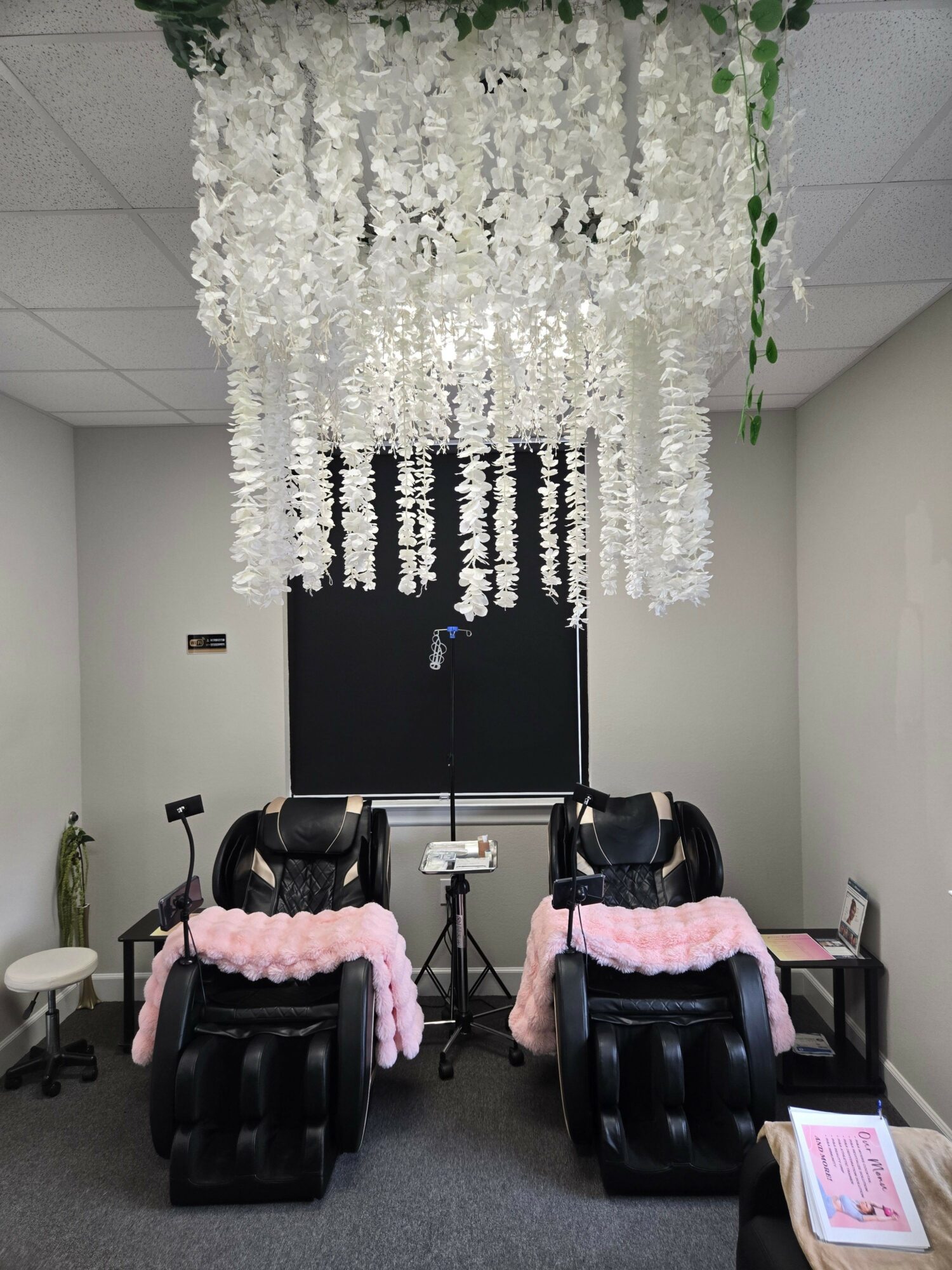 Event setup with chairs decorated with pink balloons, a floral backdrop, and a black backdrop with white text.
