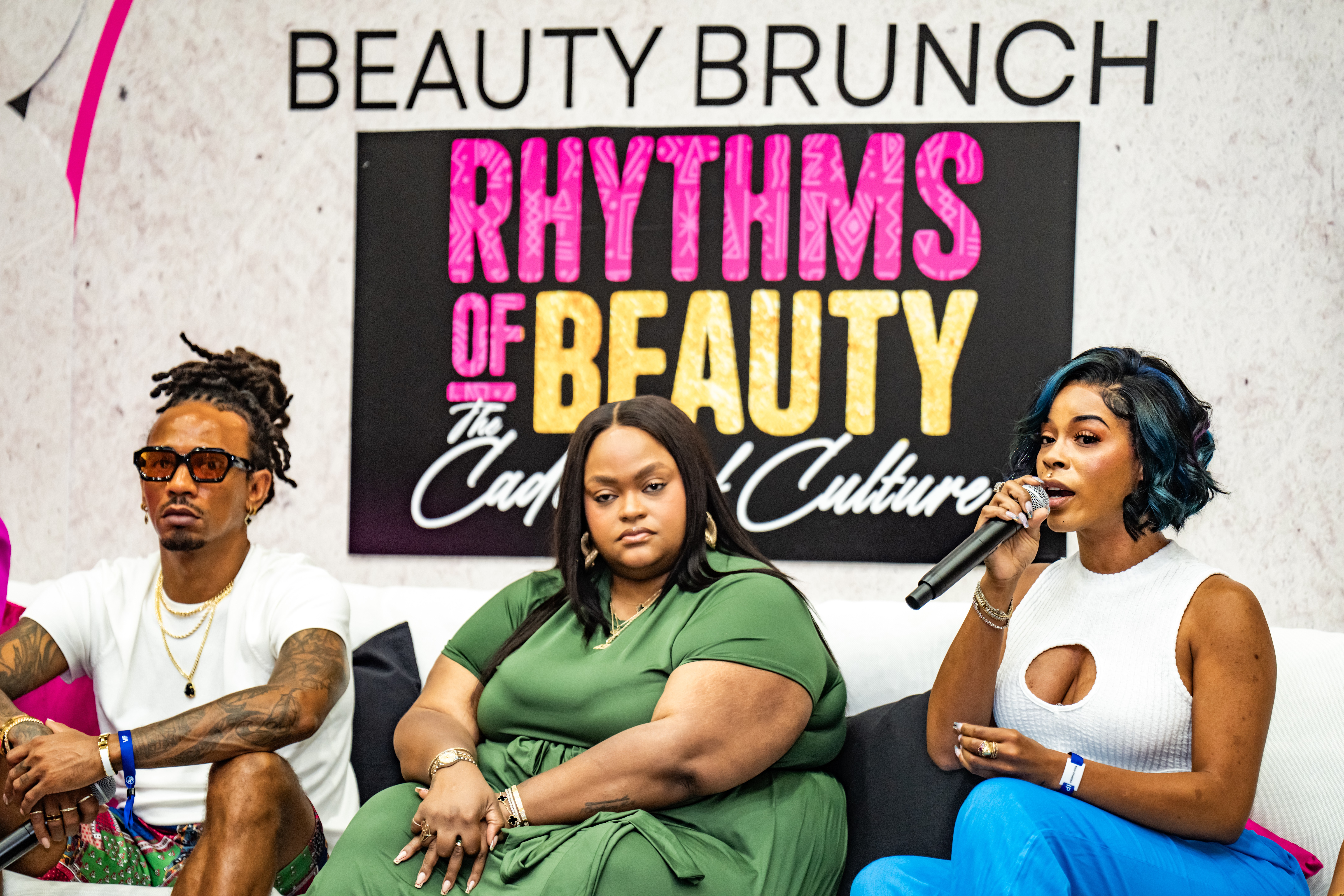 Three women seated at a panel discussion with a sign behind them reading 'Beauty Brunch Rhythms of Beauty' in pink, yellow, and white text.