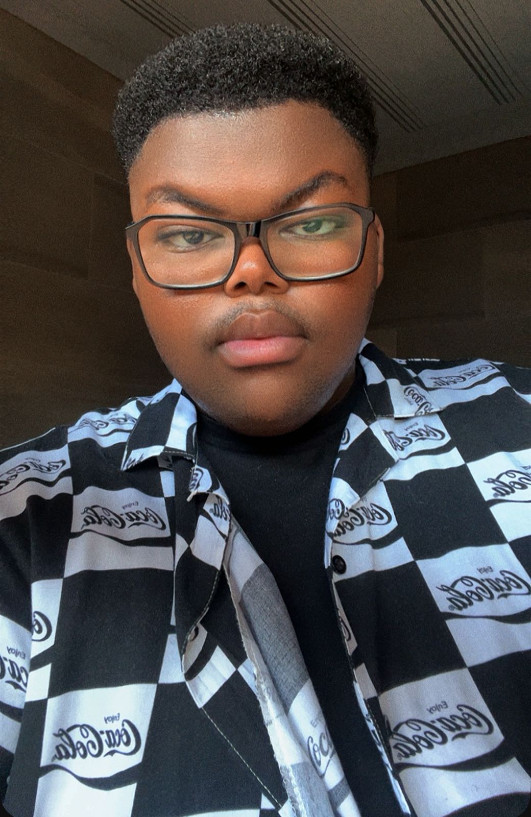 Person with short curly hair and glasses wearing a black and white checkered shirt, looking directly at the camera.